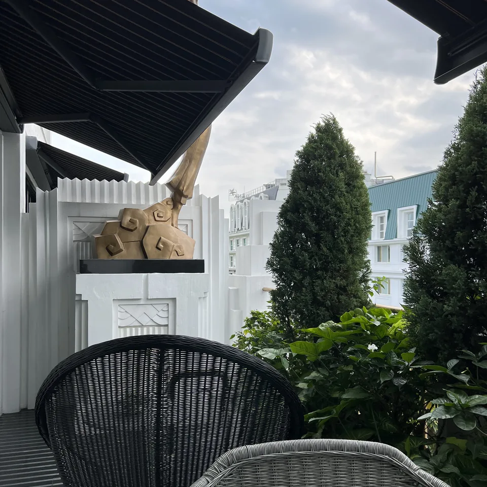 Black woven chairs under an awning on a suite terrace, with trees and the sky beyond