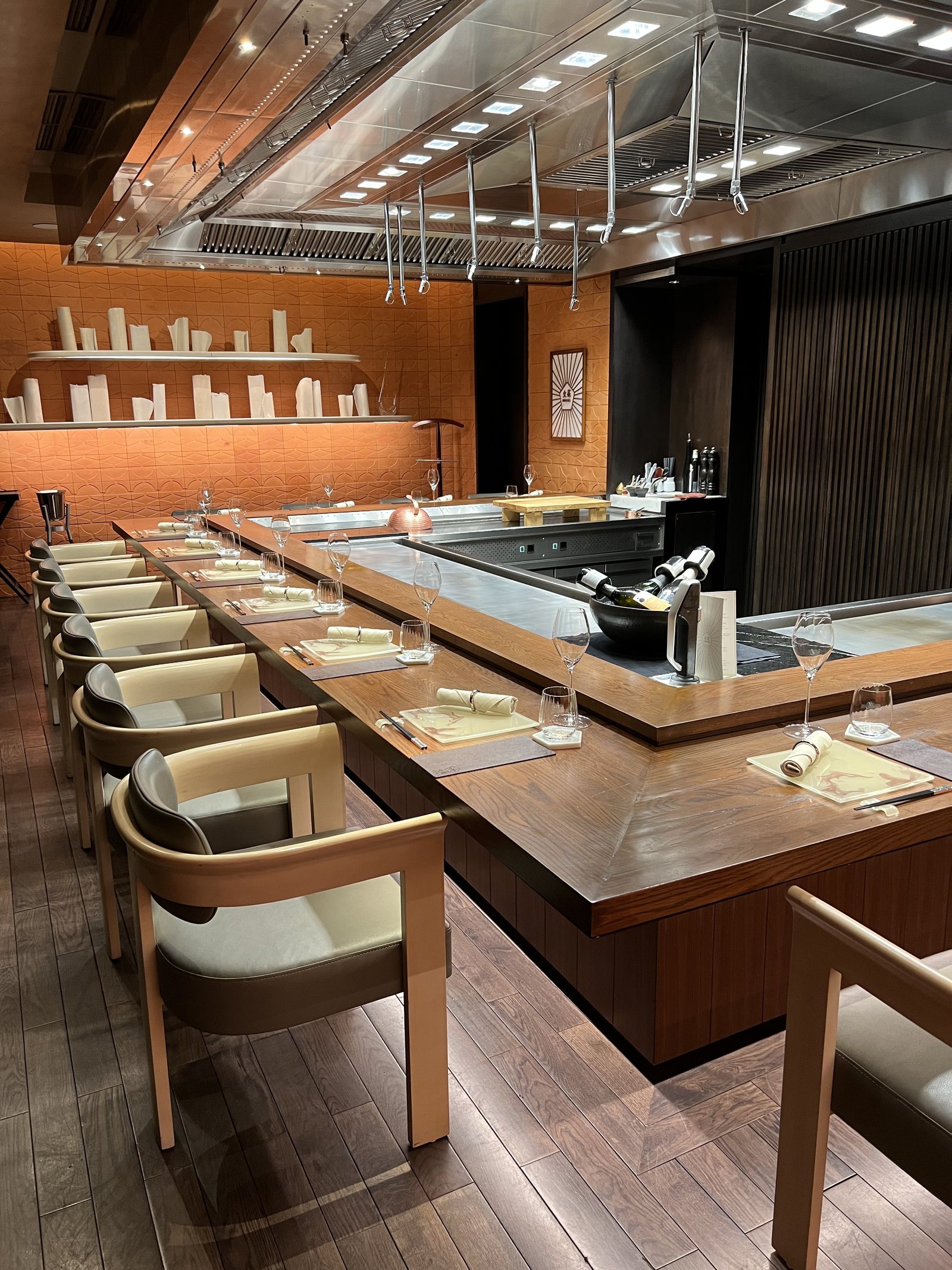 A teppanyaki counter in pale wood with chairs set around three sides and a steel plate at the centre