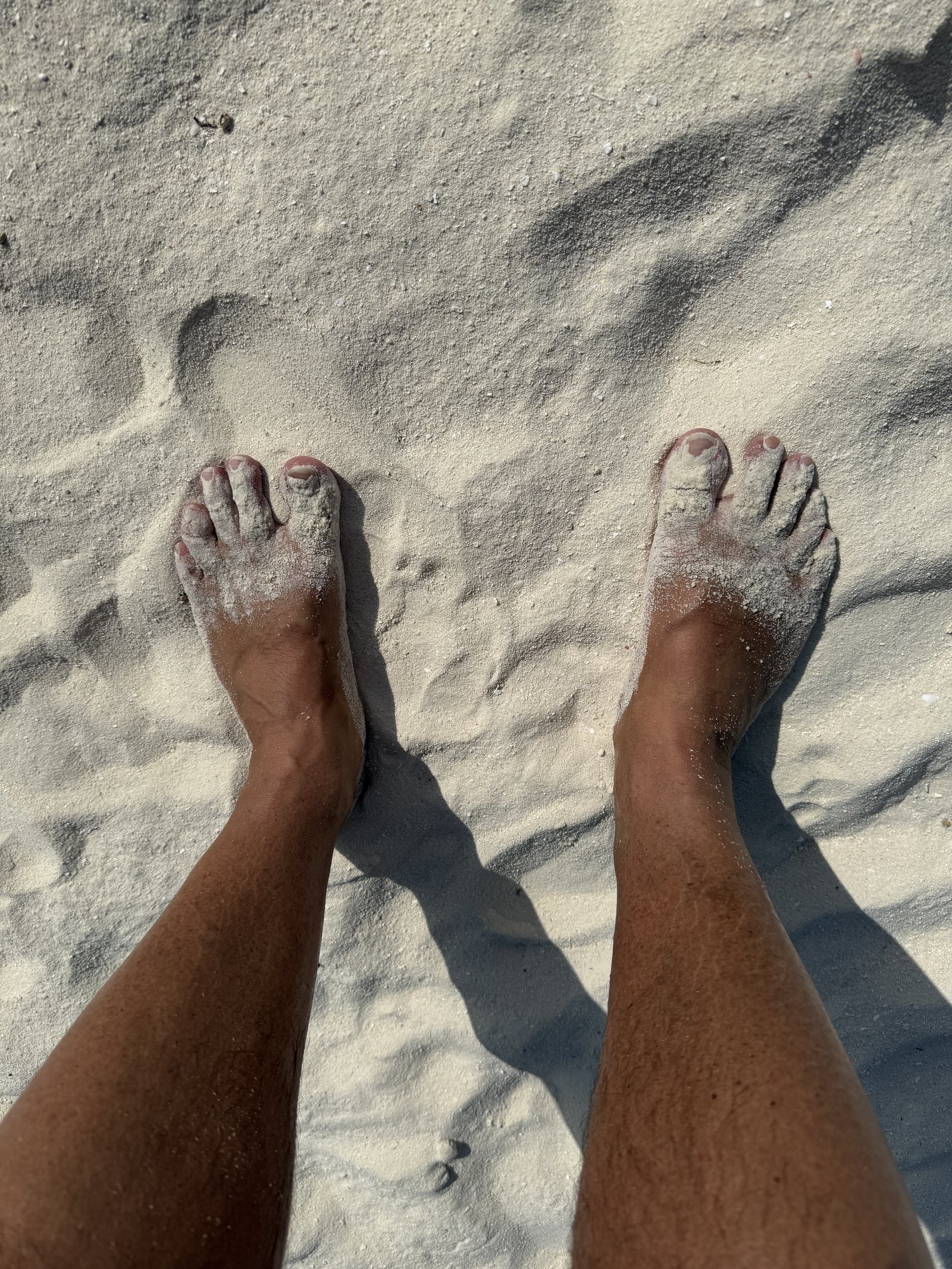 Two bare feet from above on white sand, the sand dusted over the skin