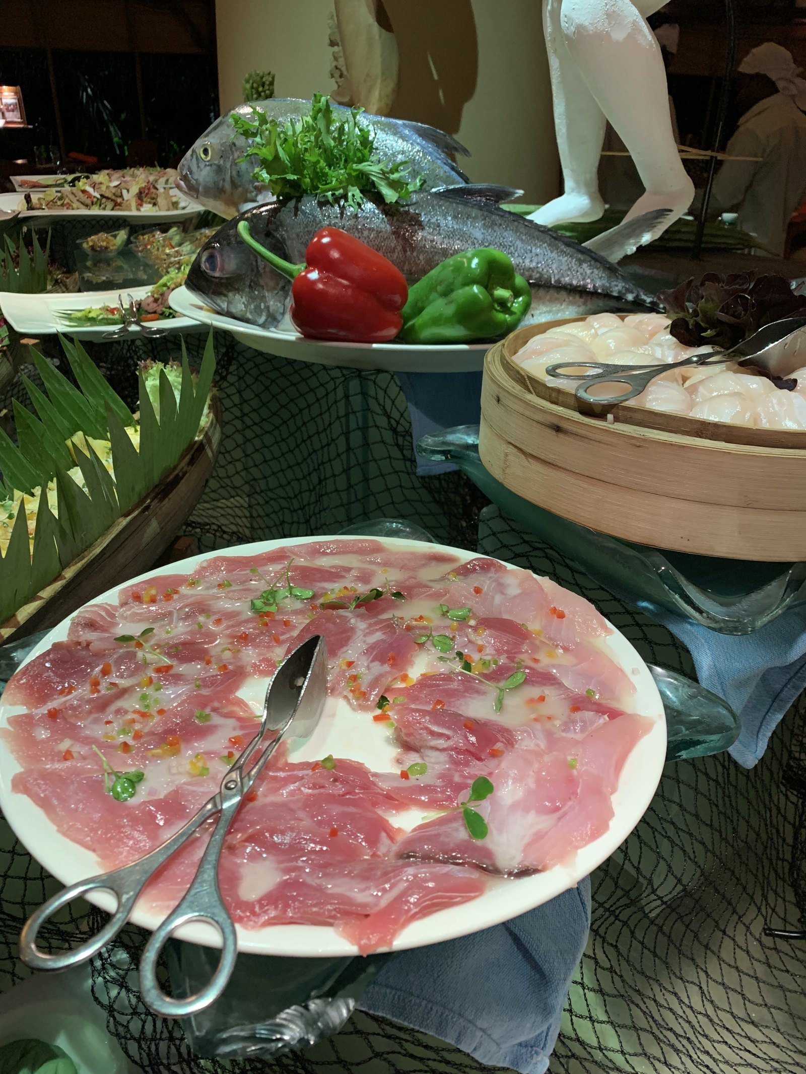 A buffet counter at Coco Palm Dhuni Kolhu with a whole fish on ice, peppers and a plate of fish carpaccio with a pair of scissors beside it