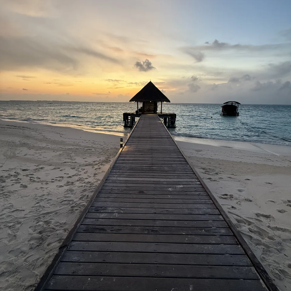 The timber jetty running out from the beach to a thatched pavilion, the sun going down behind it