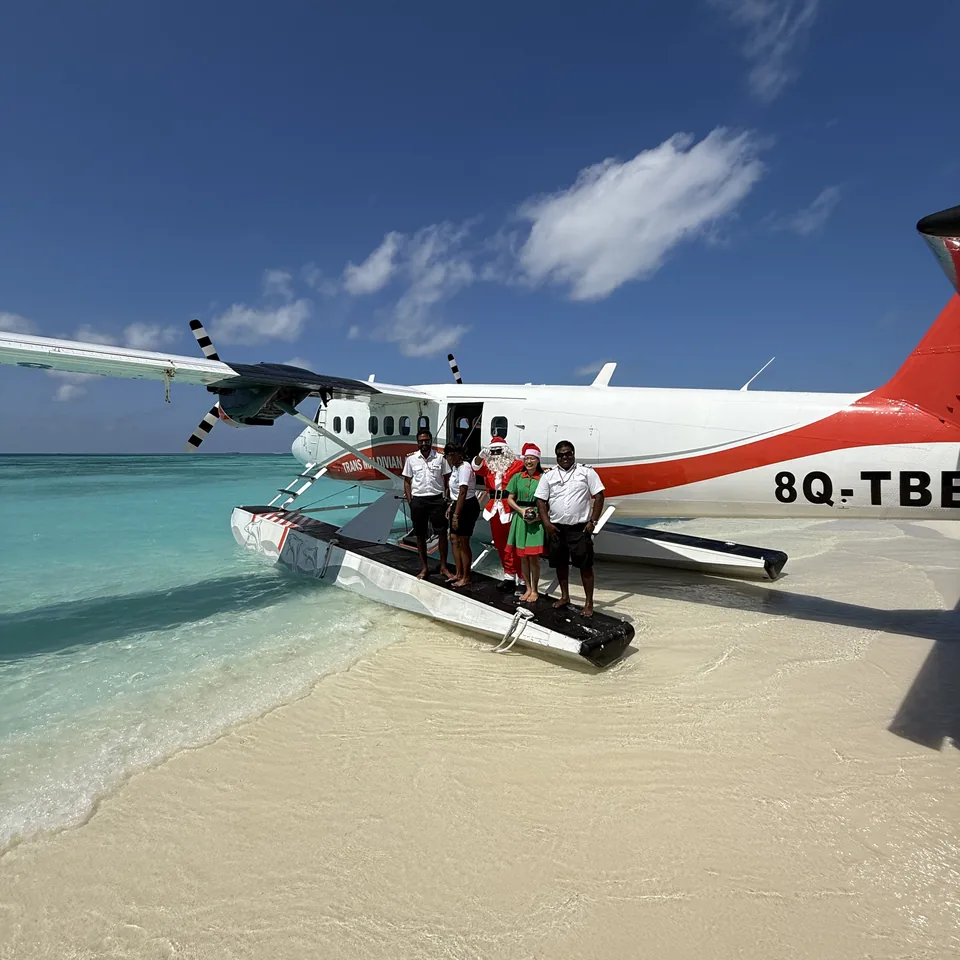 A red and white seaplane pulled up at the edge of the beach at Coco Palm Dhuni Kolhu, the crew standing on its float beside a small boat