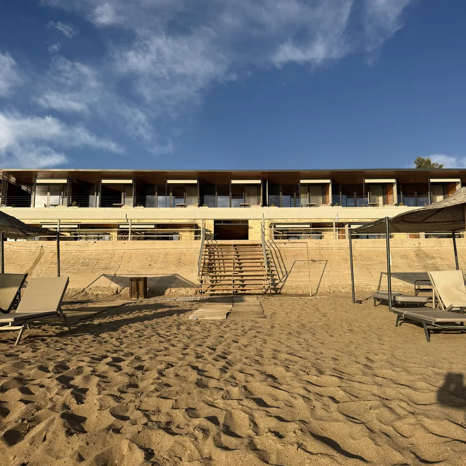 The low concrete and timber building at Dexamenes seen across the sand at dusk, beach furniture in front of it