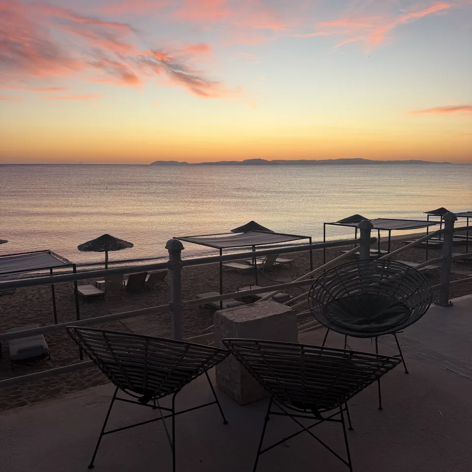 Thatched umbrellas and wire chairs on the sand at Dexamenes with the Ionian flat and the sky pink after sundown
