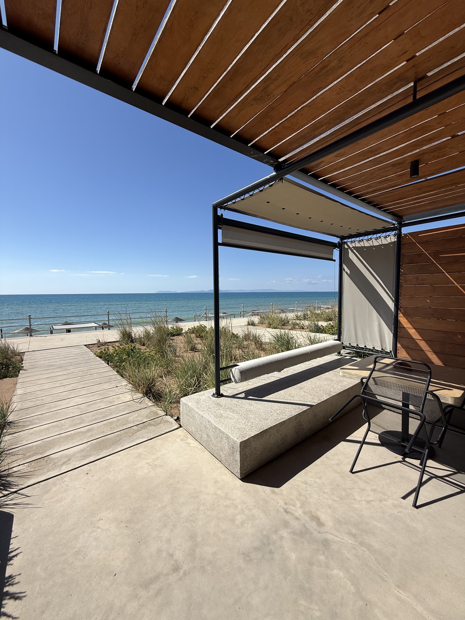 A timber boardwalk running from the terrace at Dexamenes through dune grass towards the beach and the sea