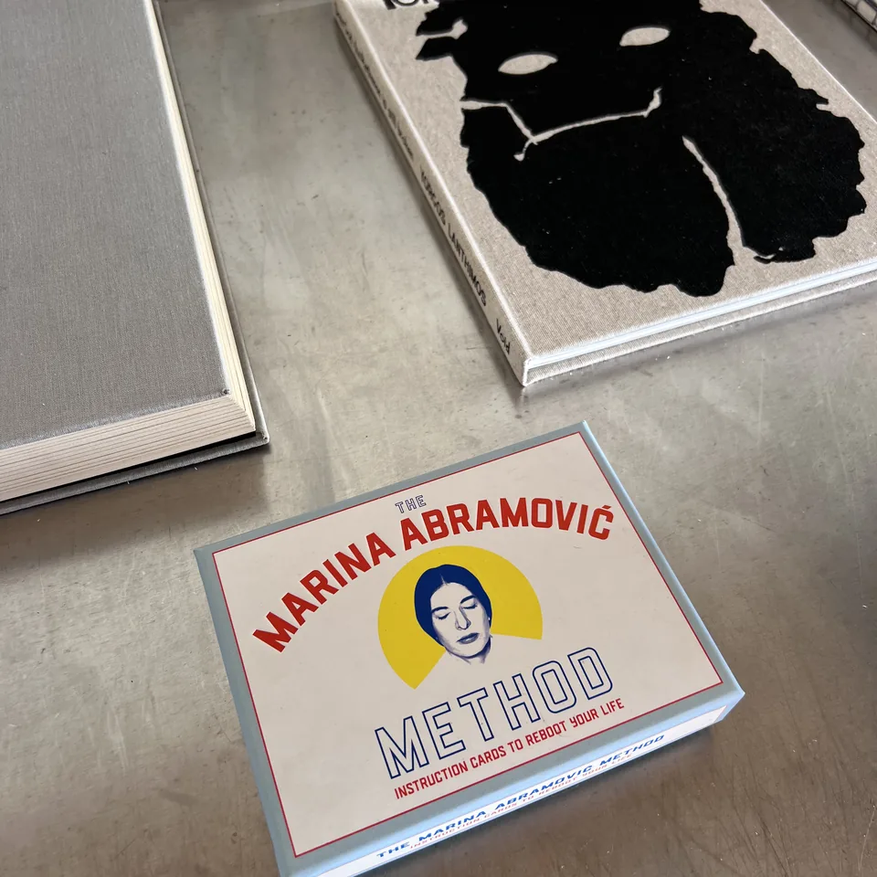 Art books stacked on a concrete surface at Dexamenes, a boxed Marina Abramovic set among them