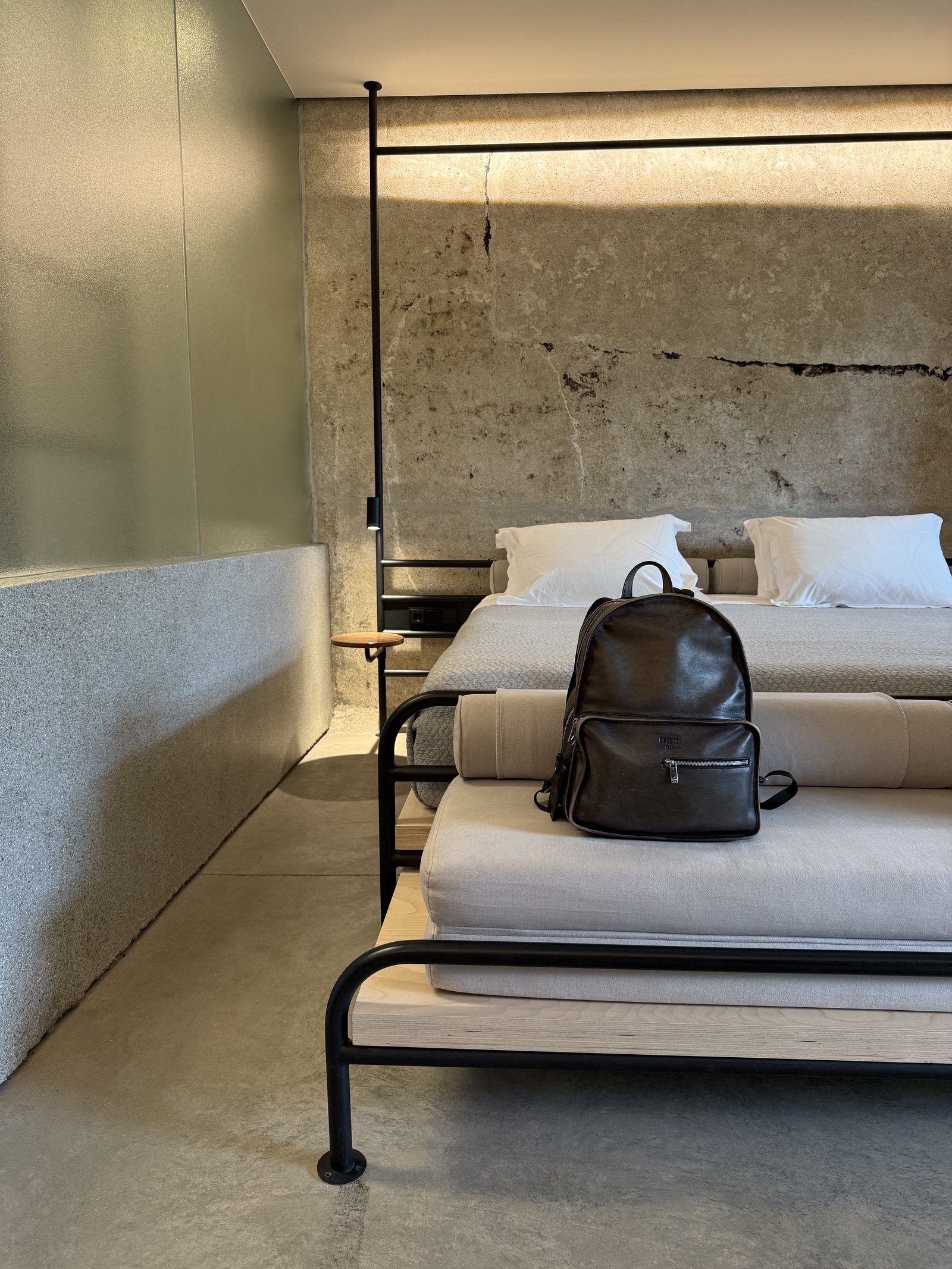 A bed against a raw concrete wall at Dexamenes, a long crack running across the concrete above the headboard