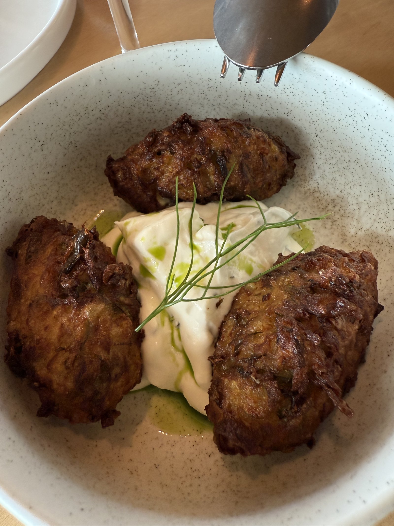 Three fried fritters on a bed of white cream with fine herbs, in a pale ceramic bowl at Dexamenes