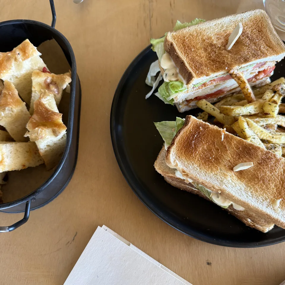 A club sandwich and a bowl of focaccia on black plates on a timber table at the beach bar at Dexamenes