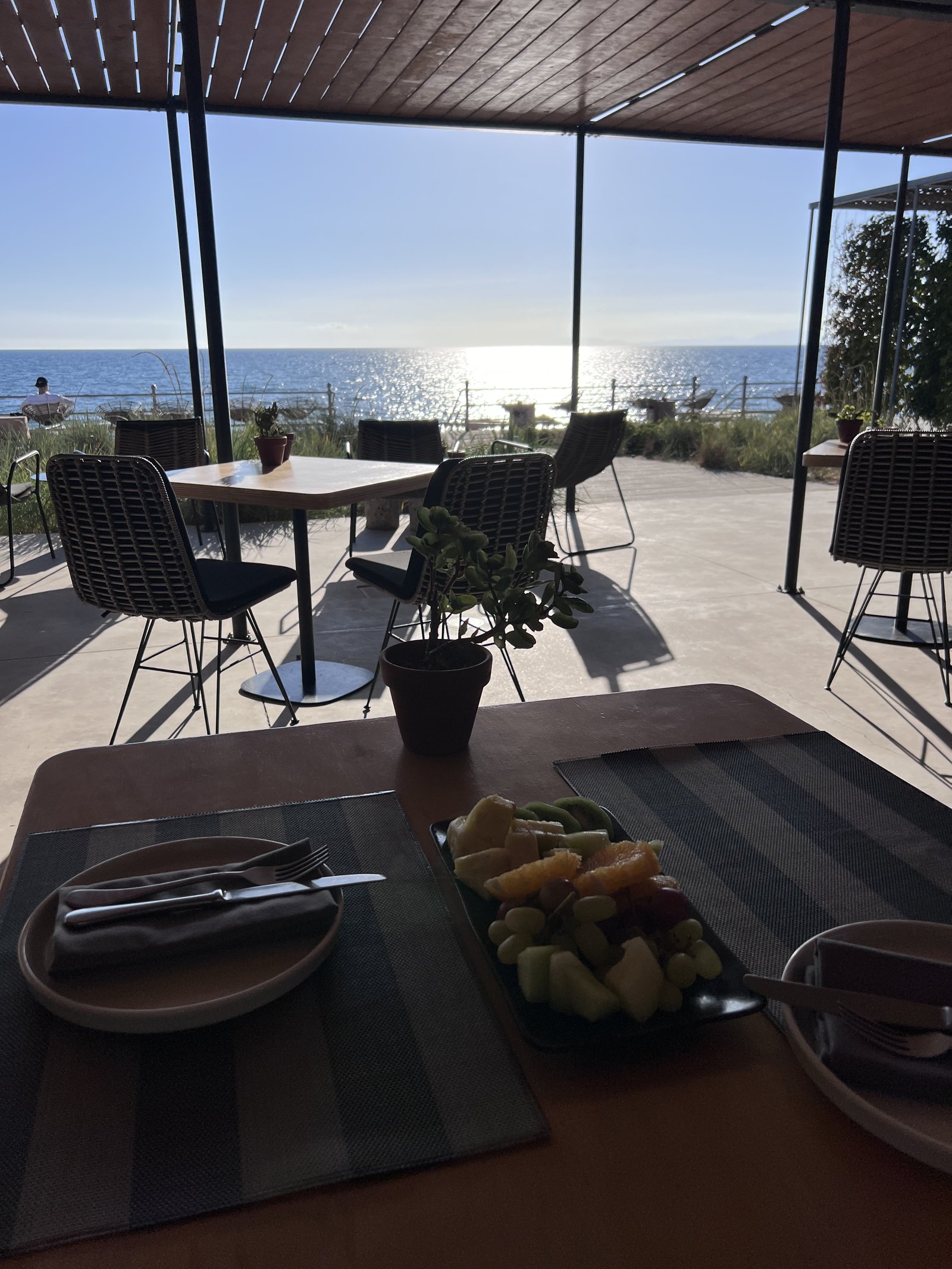 A table laid with a platter and glasses at Dexamenes, the covered terrace opening to the flat sea and the sun on the water