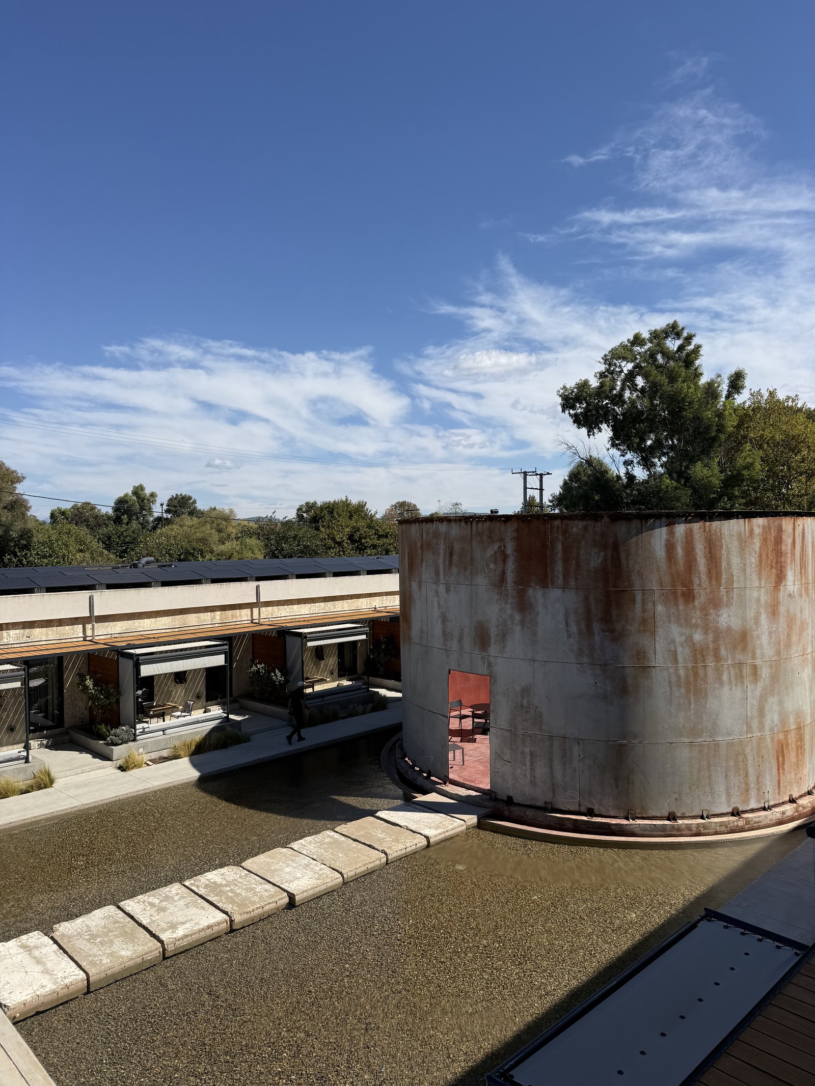 Looking down from a terrace at Dexamenes onto a rusted tank, the long low line of suites behind it and trees beyond