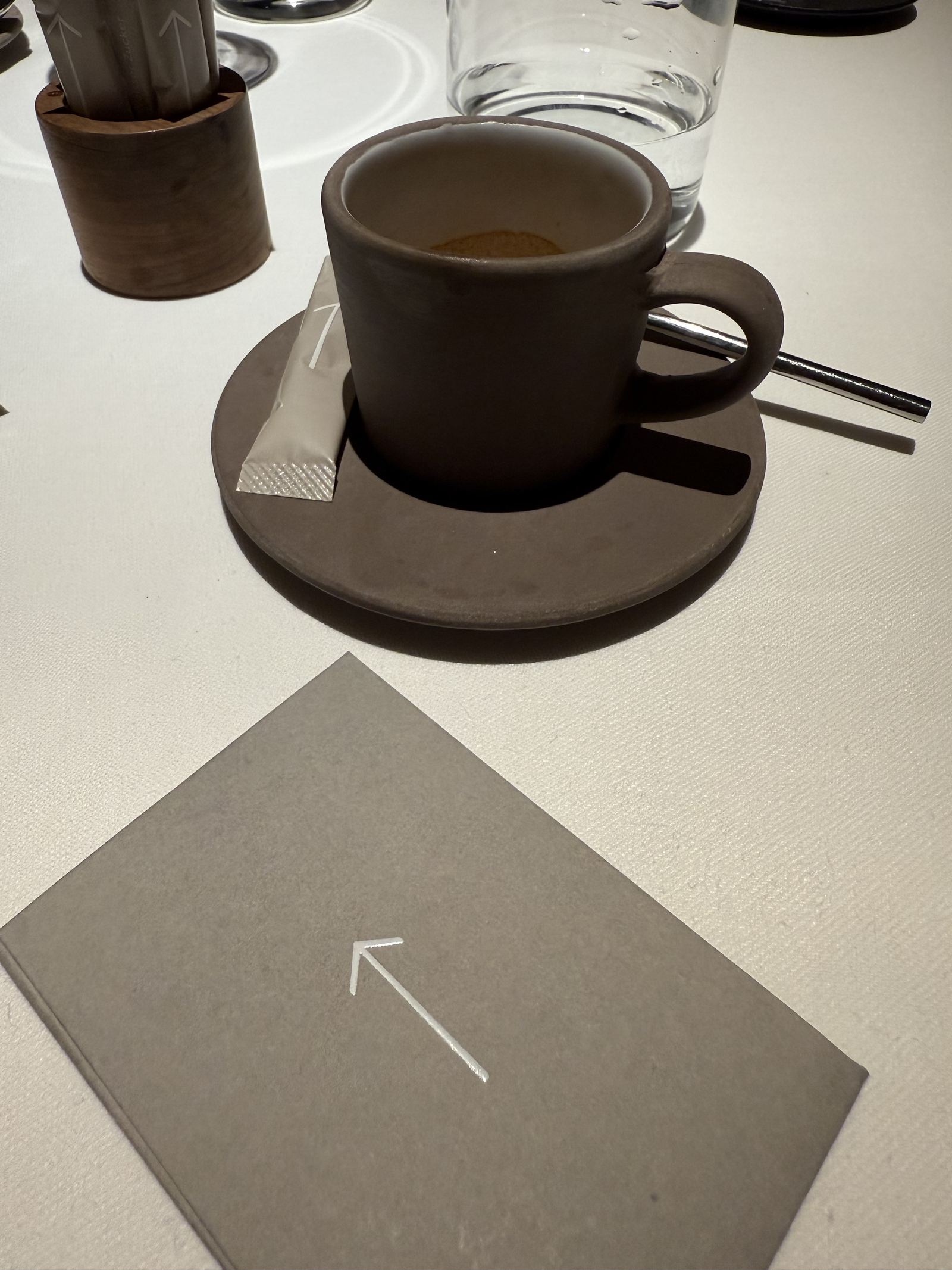 An espresso on a dark saucer beside a grey card printed with the FORESTIS arrow