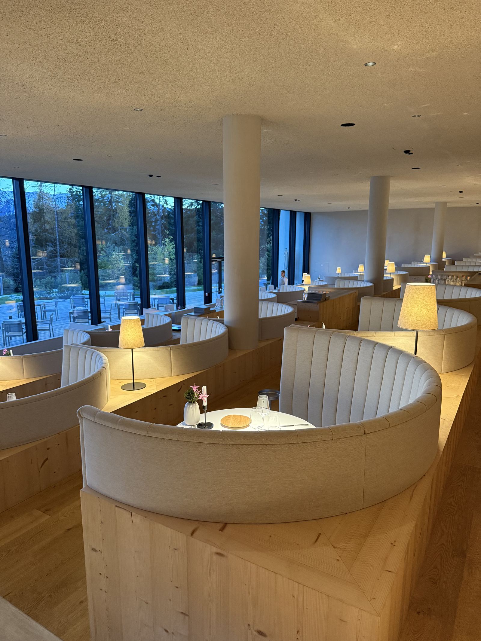 The tiered dining room at FORESTIS with lamps lit over curved banquettes