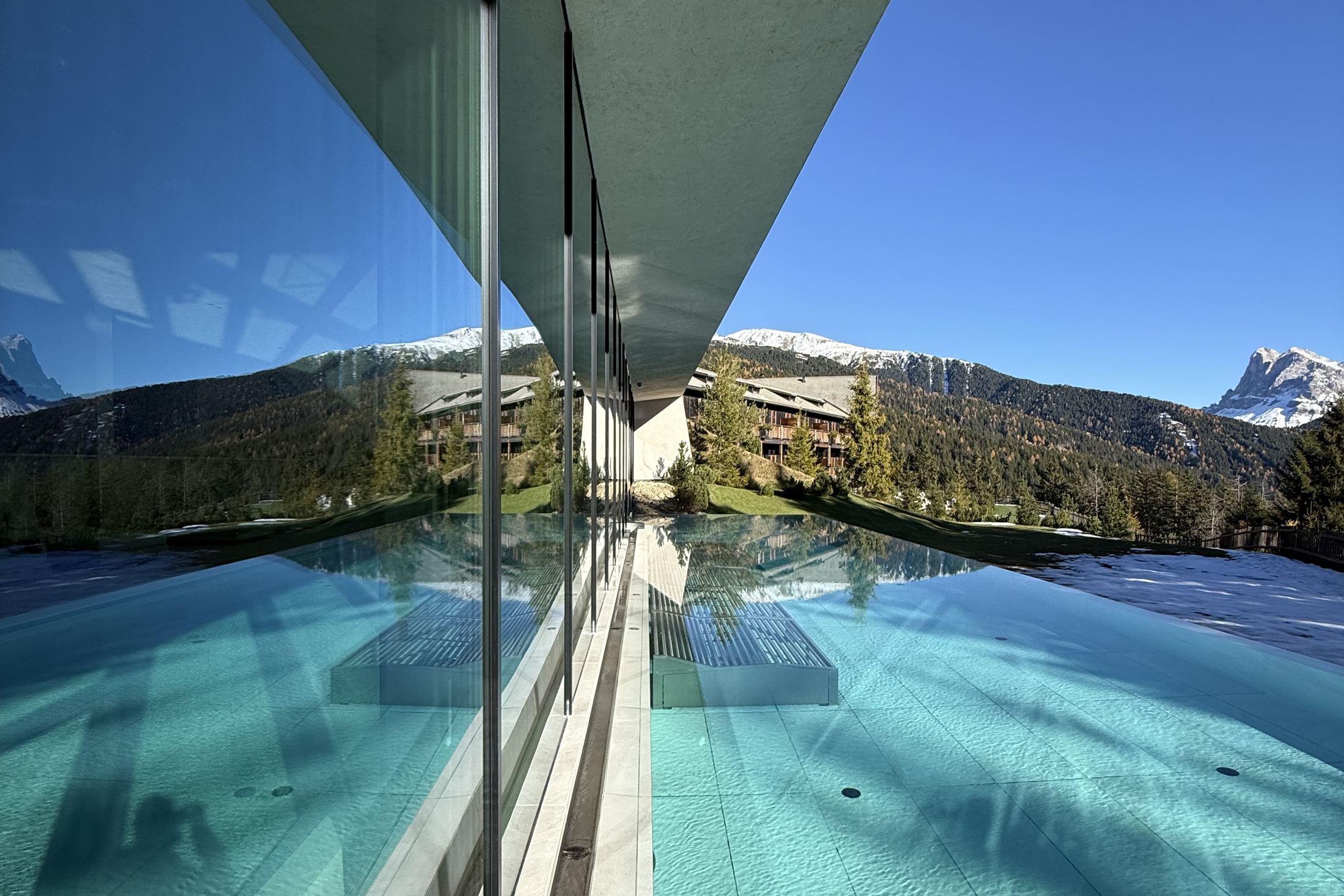 The outdoor pool at FORESTIS with the Odle reflected in the glass balustrade