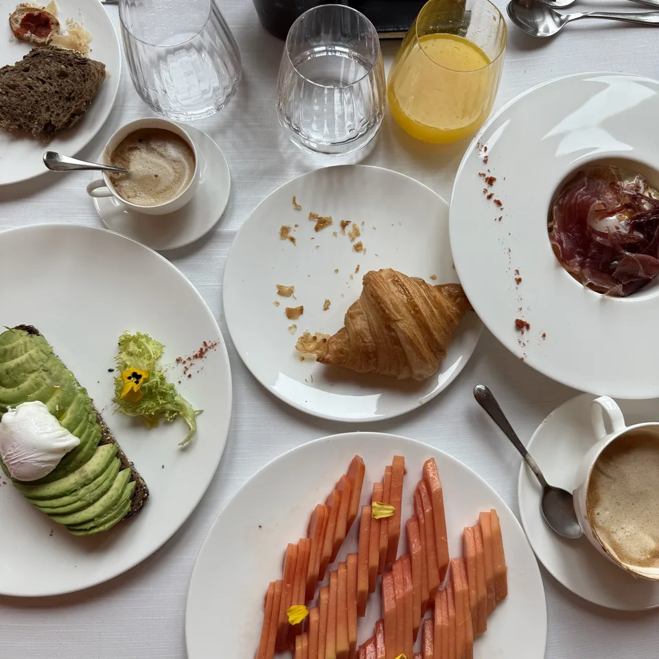 A breakfast table laid with avocado toast, salmon and a croissant