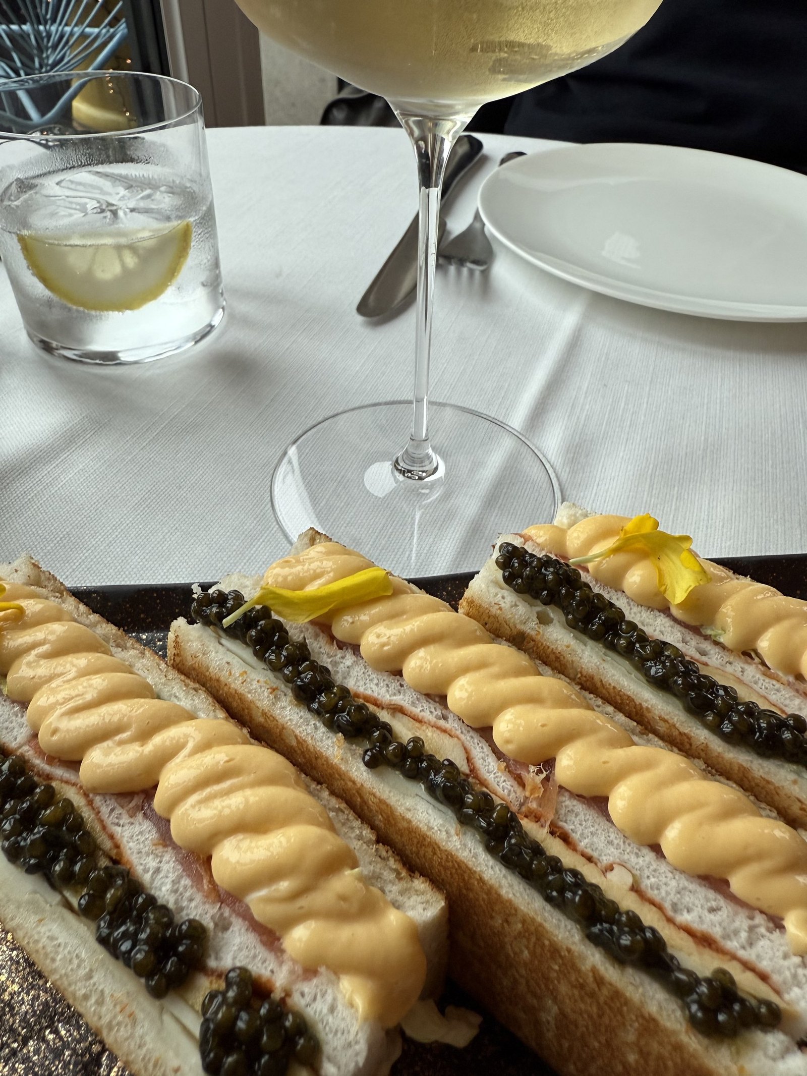 Toasts topped with caviar and a piped cream served on a white tablecloth