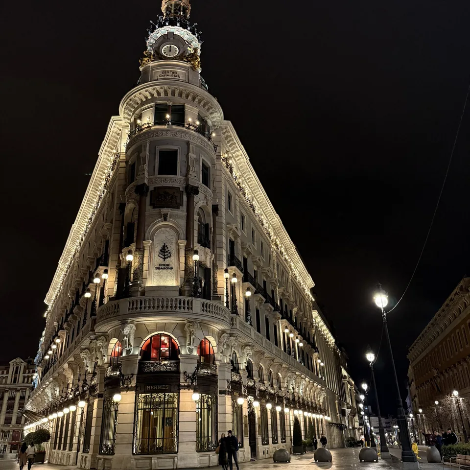 The corner facade of Four Seasons Madrid lit at night above an empty street