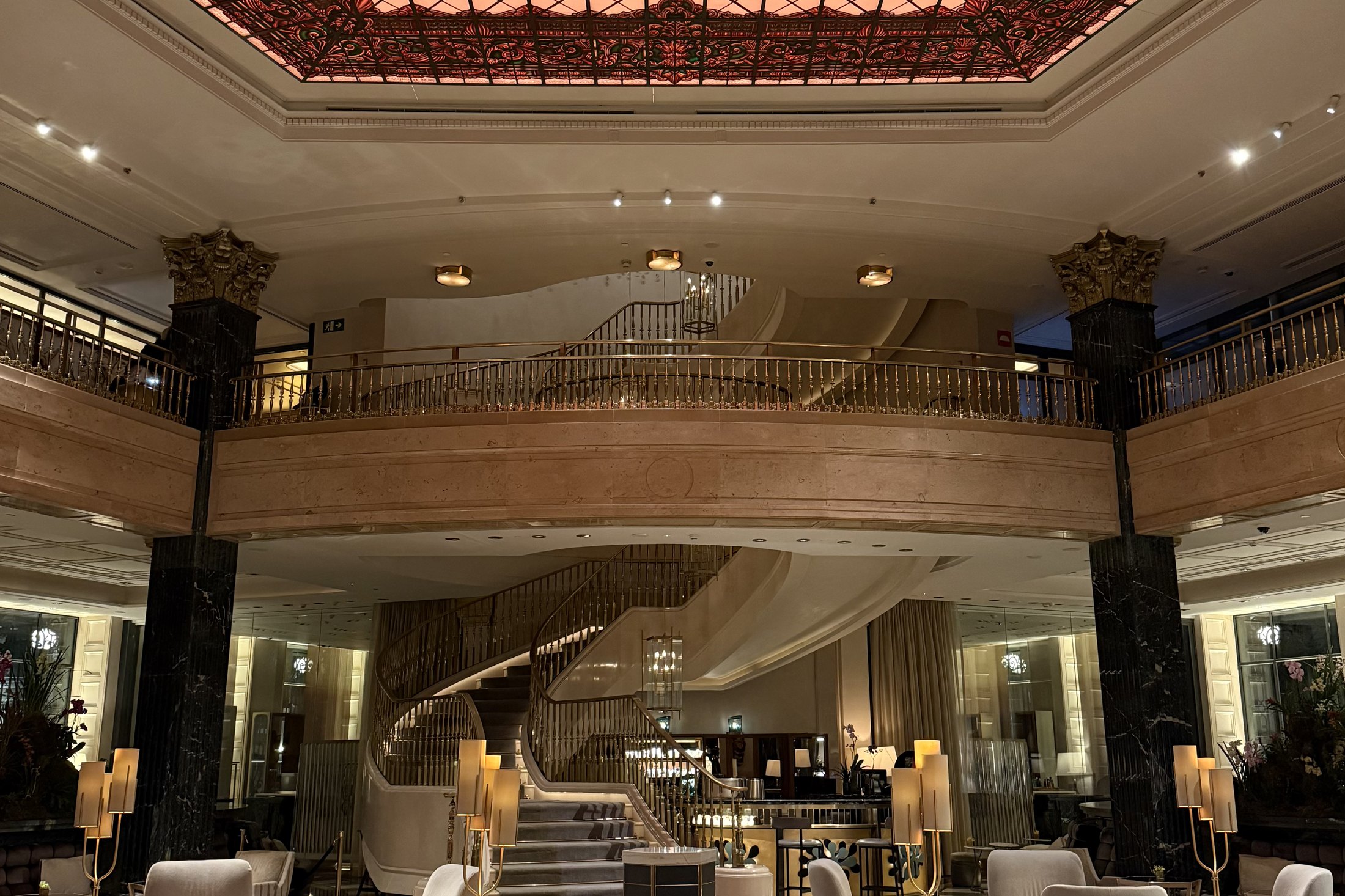 The galleria of Four Seasons Madrid under its glass roof, with the curved staircase beyond