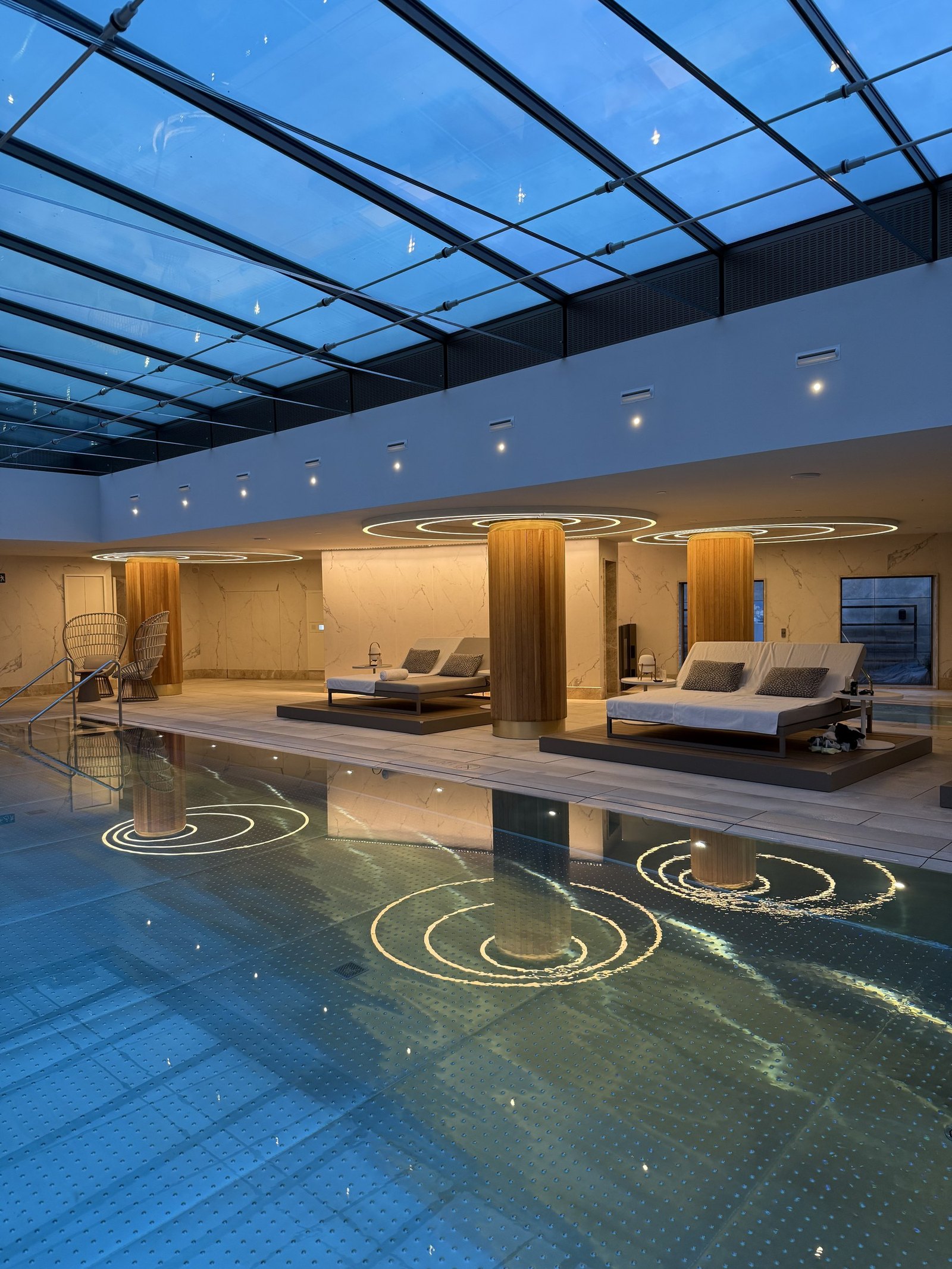 The indoor pool at dusk with the loungers and the lit ceiling rings