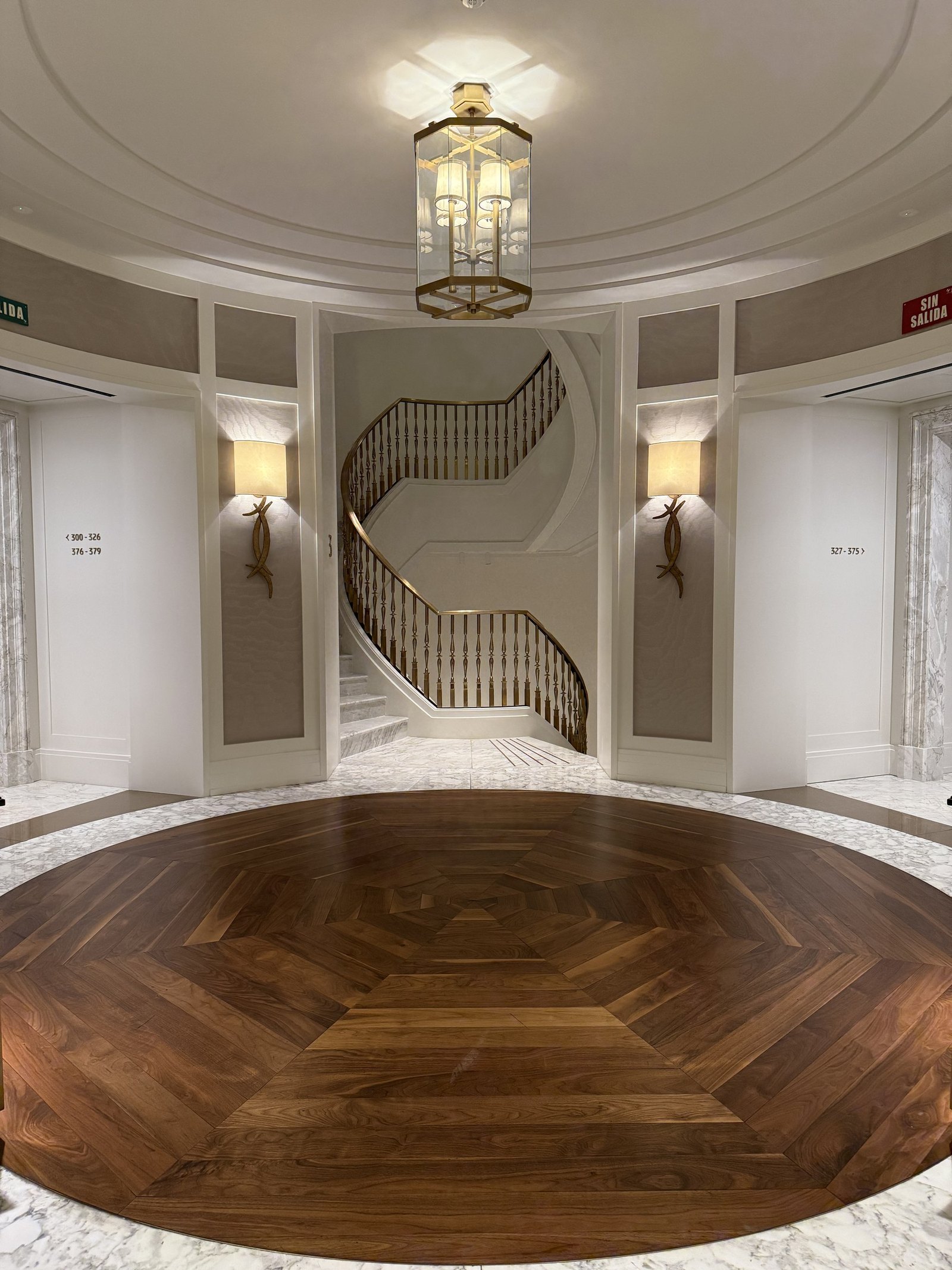 A white oval stair hall with a curved staircase and a round timber floor inlay