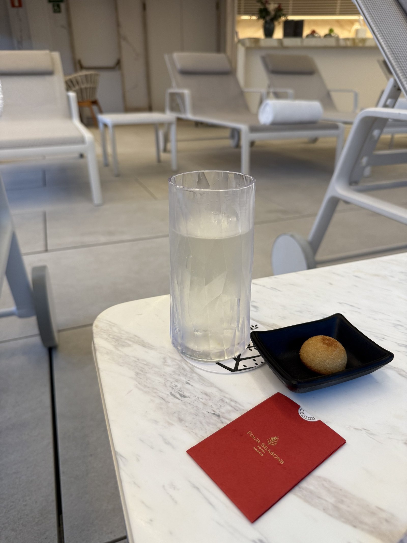 A glass of water and a small pastry on a marble table beside a spa lounger