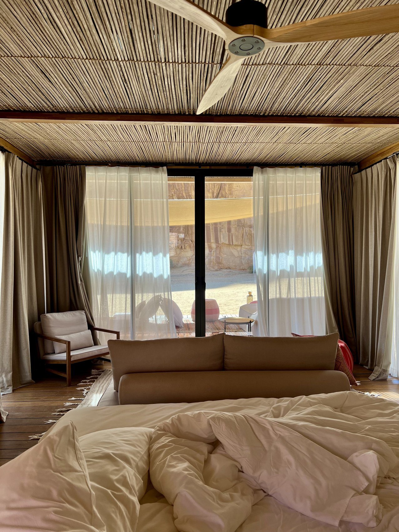 An unmade bed at Habitas AlUla with sheer curtains drawn back onto the terrace and the morning light outside