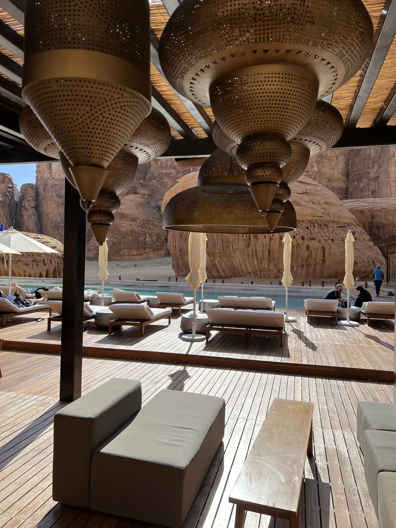 Large perforated brass pendant lamps hanging over a seating area at Habitas AlUla with the rock beyond