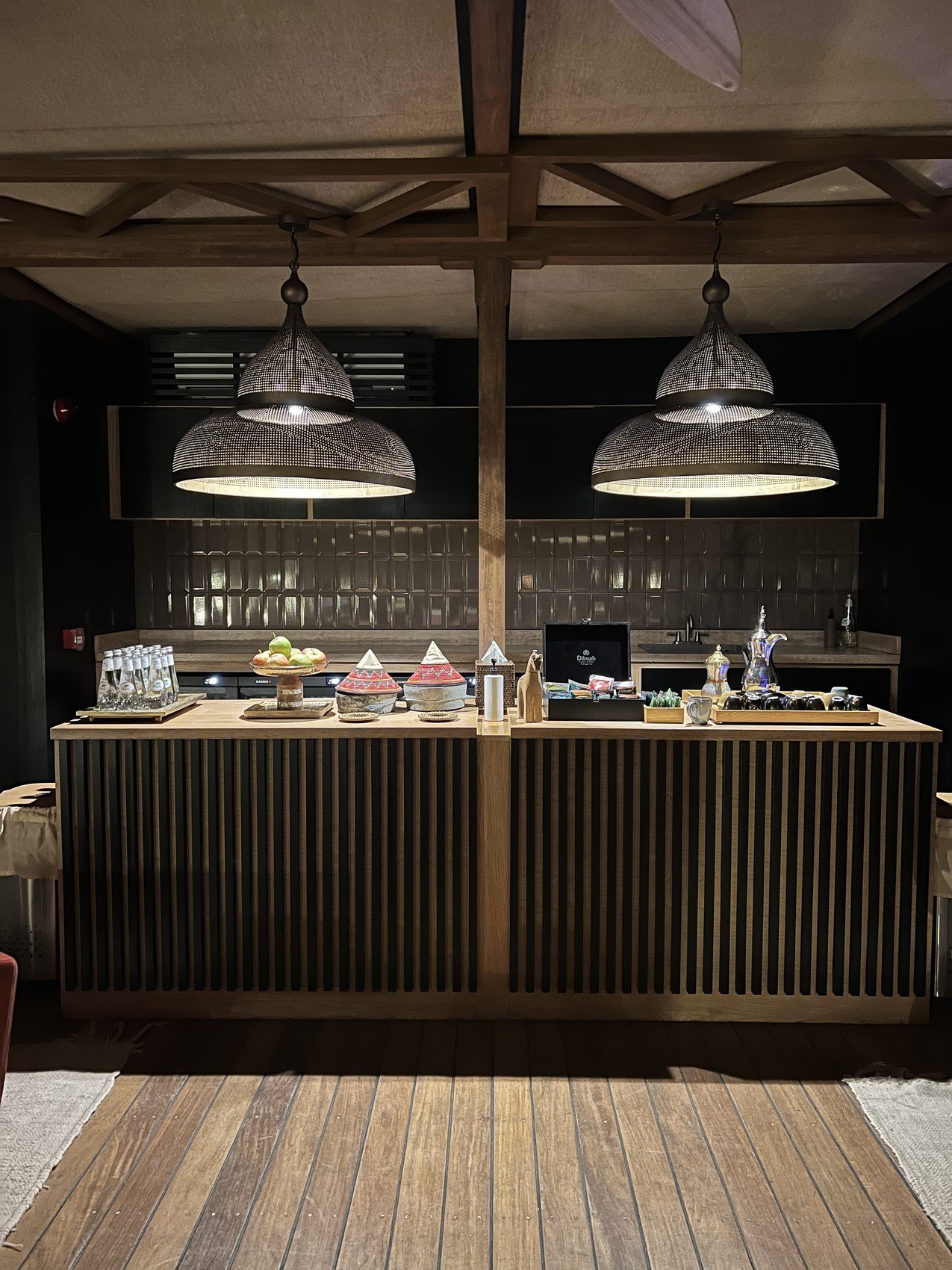 A buffet counter at Habitas AlUla under two large shaded pendant lamps with cakes and small dishes laid out