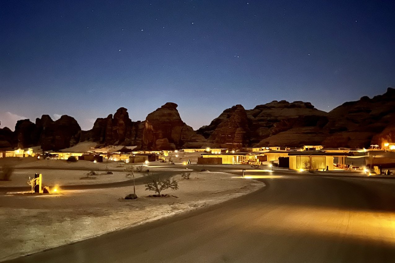 The camp at Habitas AlUla lit along the valley floor at night with the dark mass of the sandstone cliffs behind it