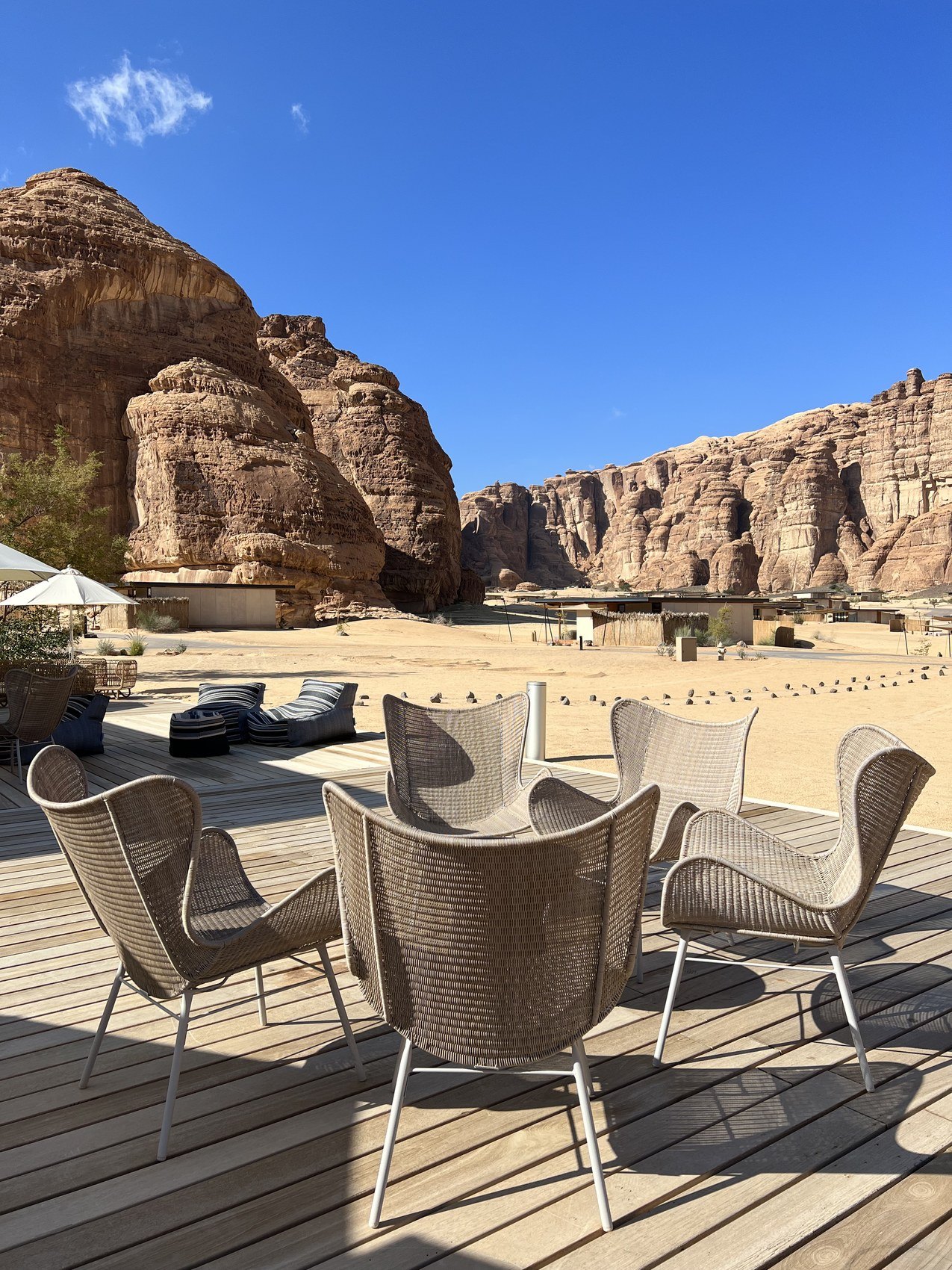 Woven chairs and a low table on a timber deck at Habitas AlUla with the sandstone formations behind