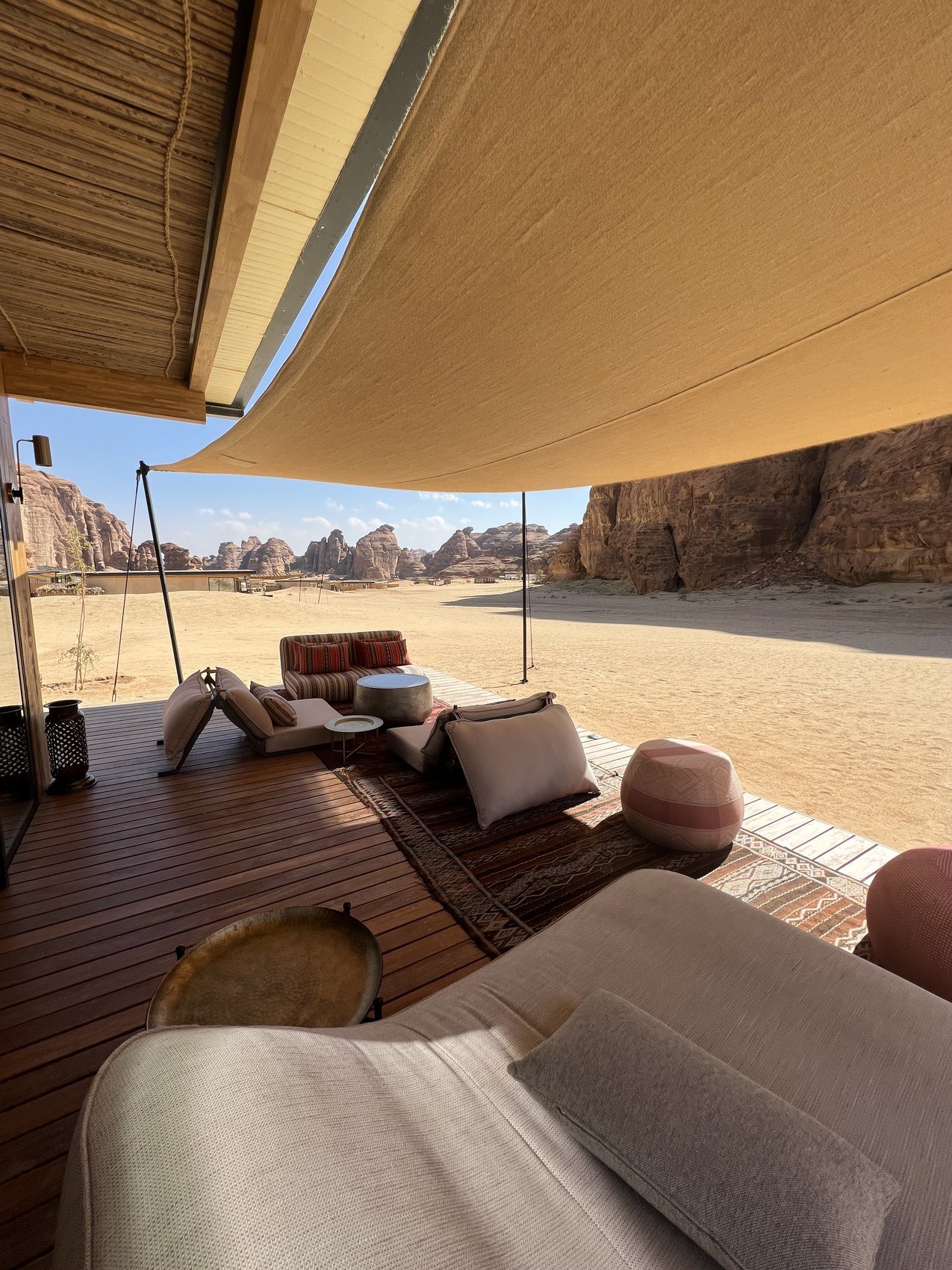 Cushions and a low table on the timber deck of a villa at Habitas AlUla, looking out across the sand to the cliffs