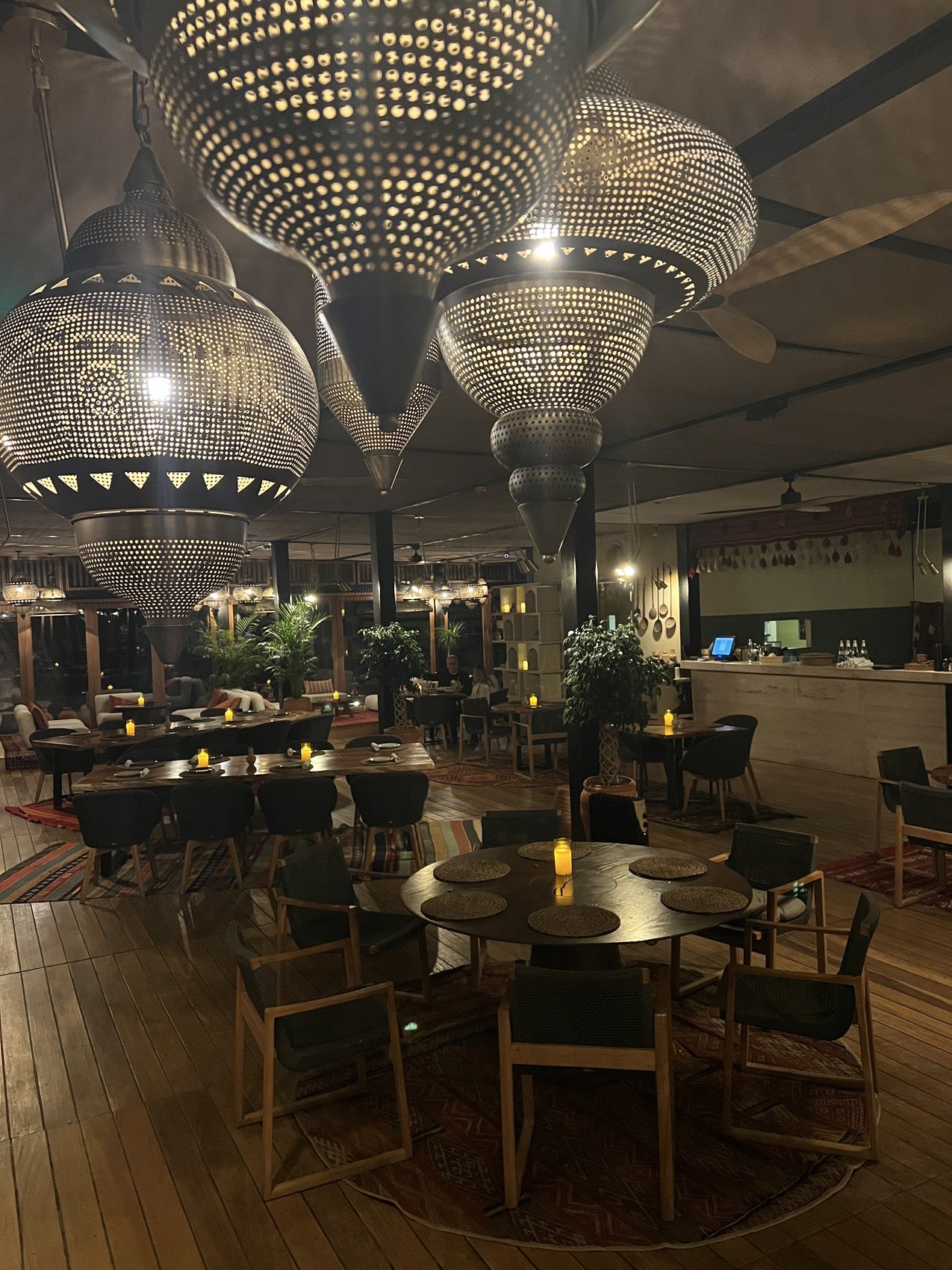 The dining room at Habitas AlUla under a ceiling of perforated metal pendant lamps with round tables and rugs