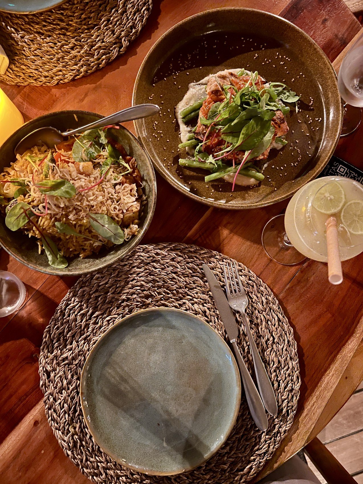 Two ceramic bowls of grain salad and greens on a timber table at Habitas AlUla with a plate and woven mats