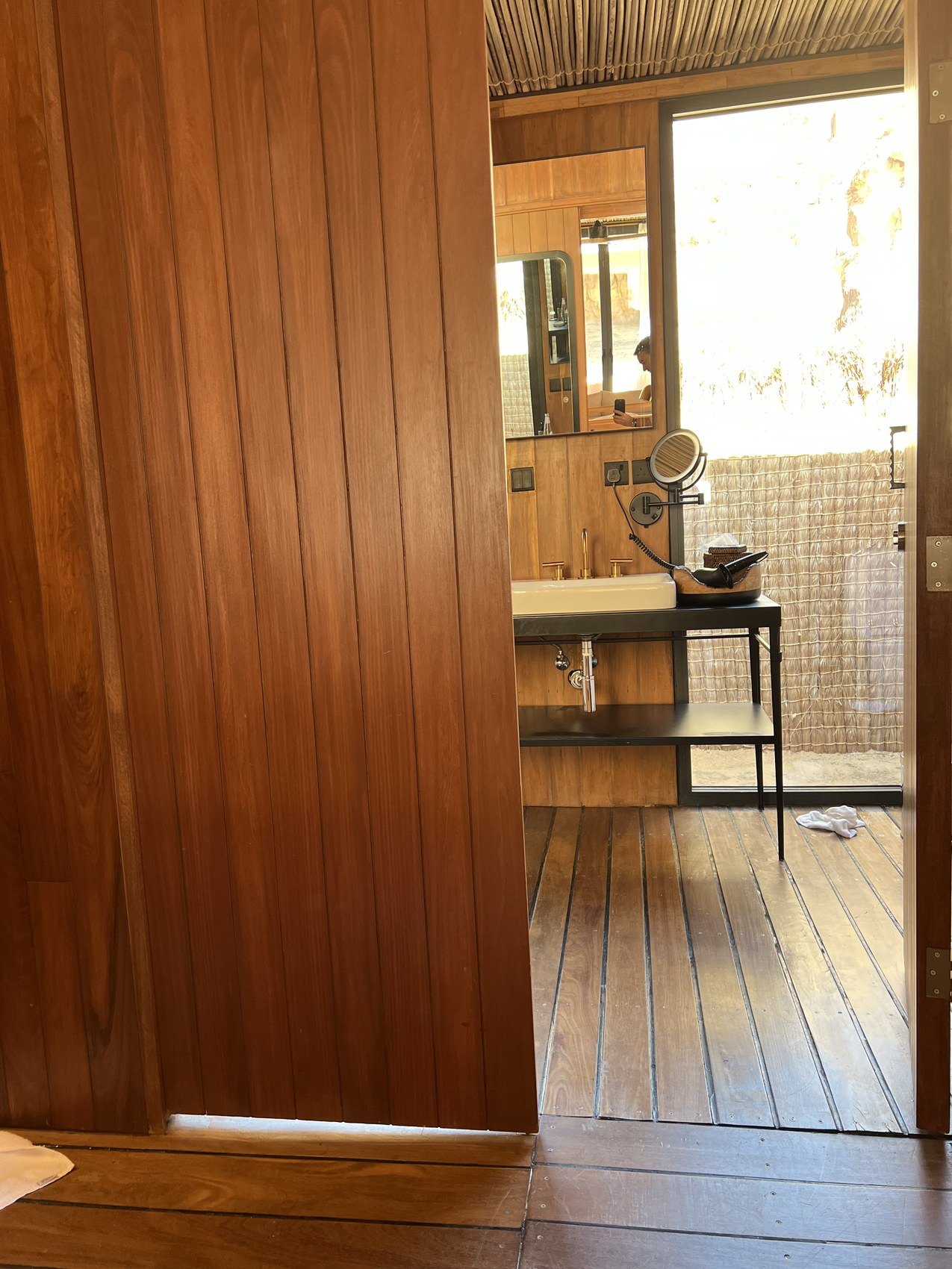 A timber door standing open onto the bathroom at Habitas AlUla with the stone basin beyond