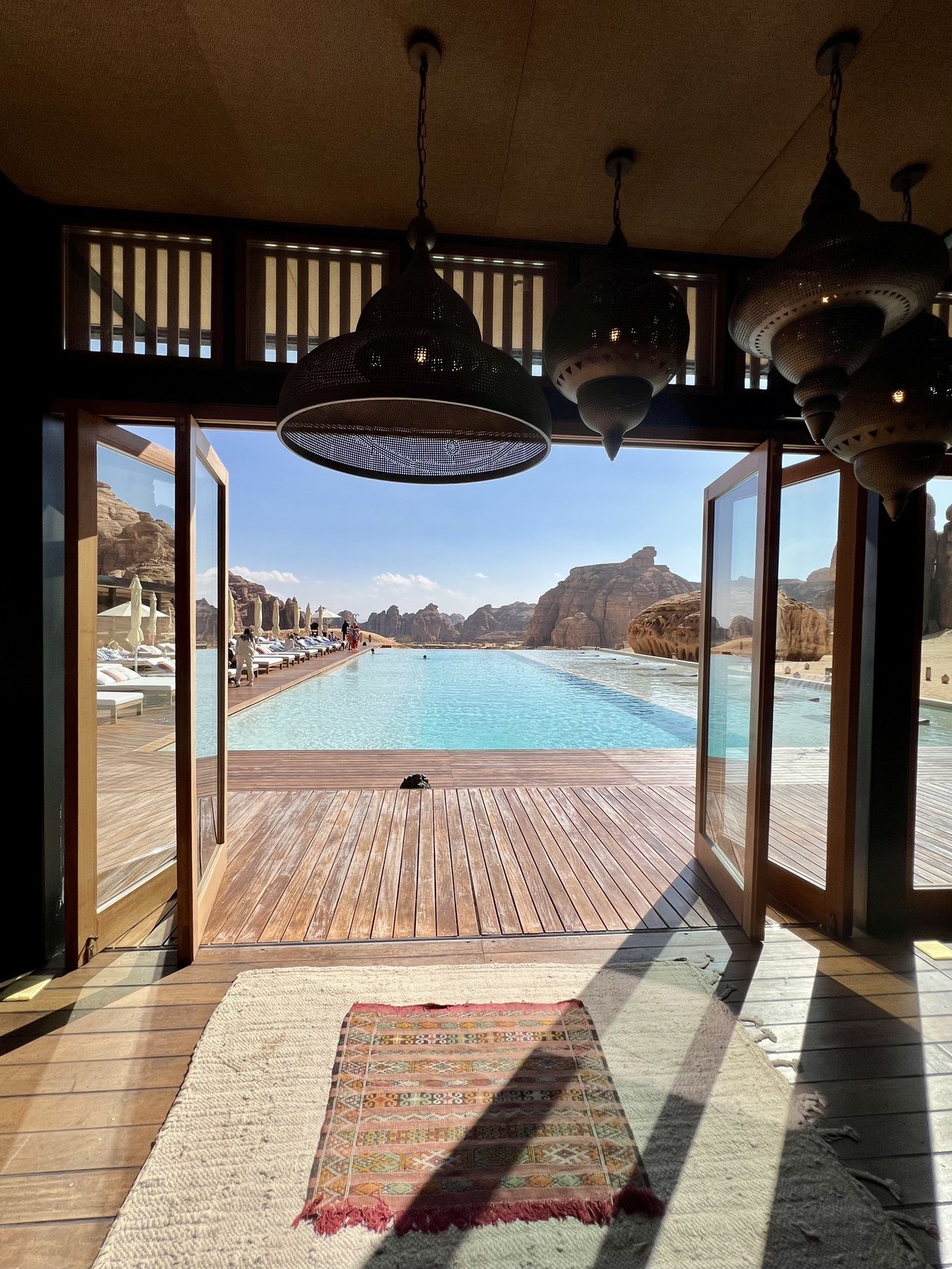 A timber doorway at Habitas AlUla framing the pool and the loungers beyond, with a kilim runner on the floor