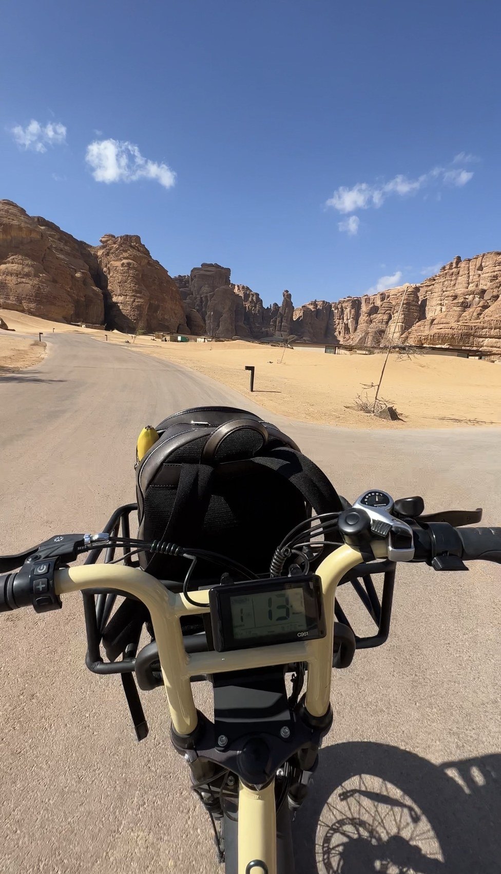 The handlebars of an electric bicycle on a desert road at AlUla with sandstone formations ahead