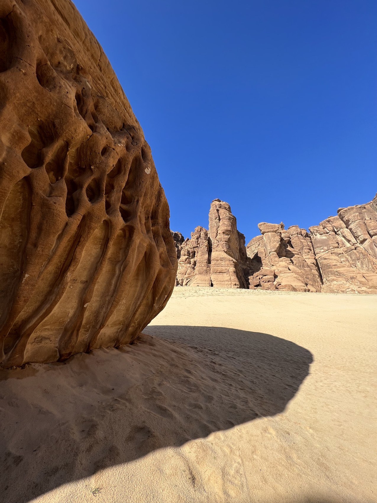 A sandstone outcrop throwing a hard shadow across pale sand under a deep blue sky