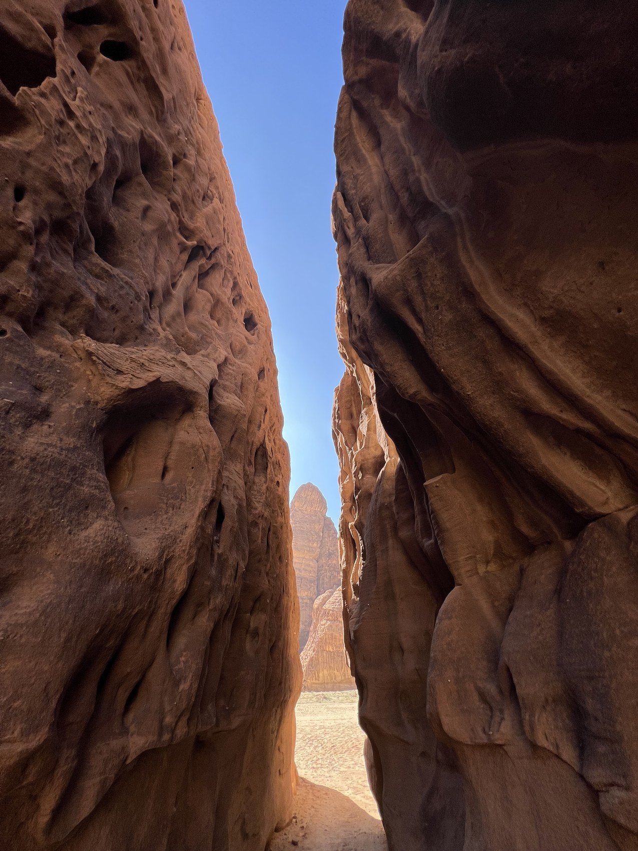 A narrow gap between two sandstone walls at AlUla opening onto a strip of blue sky