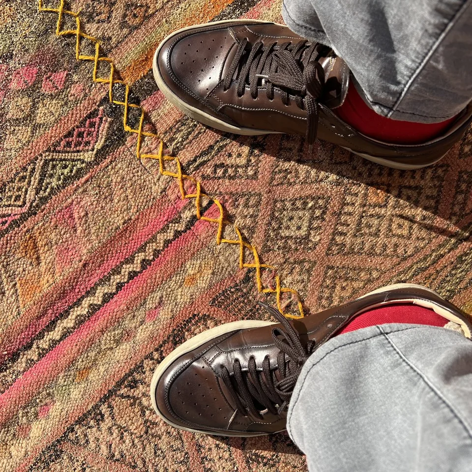 Dark leather sneakers seen from above on a red kilim laid over the sand at Habitas AlUla