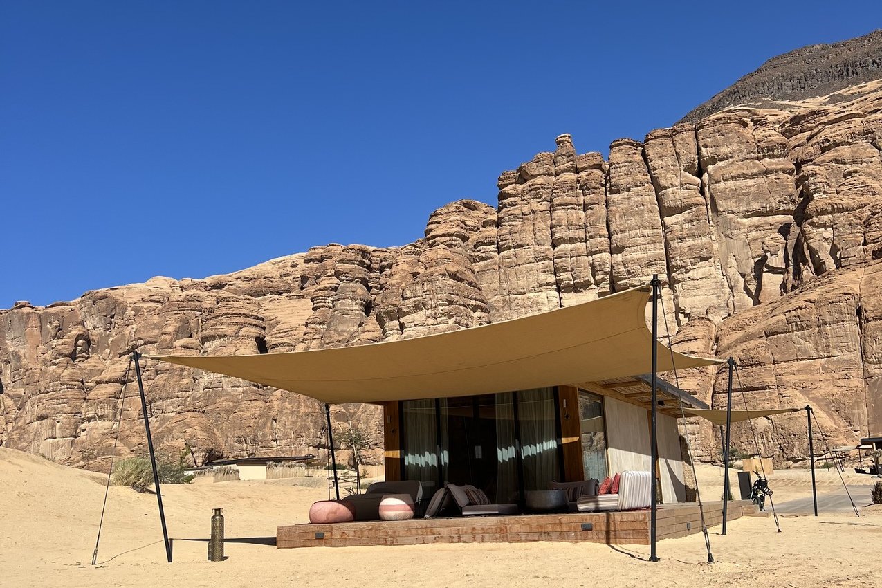 A tented villa at Habitas AlUla standing under a stretched canopy with the sandstone cliff rising directly behind it