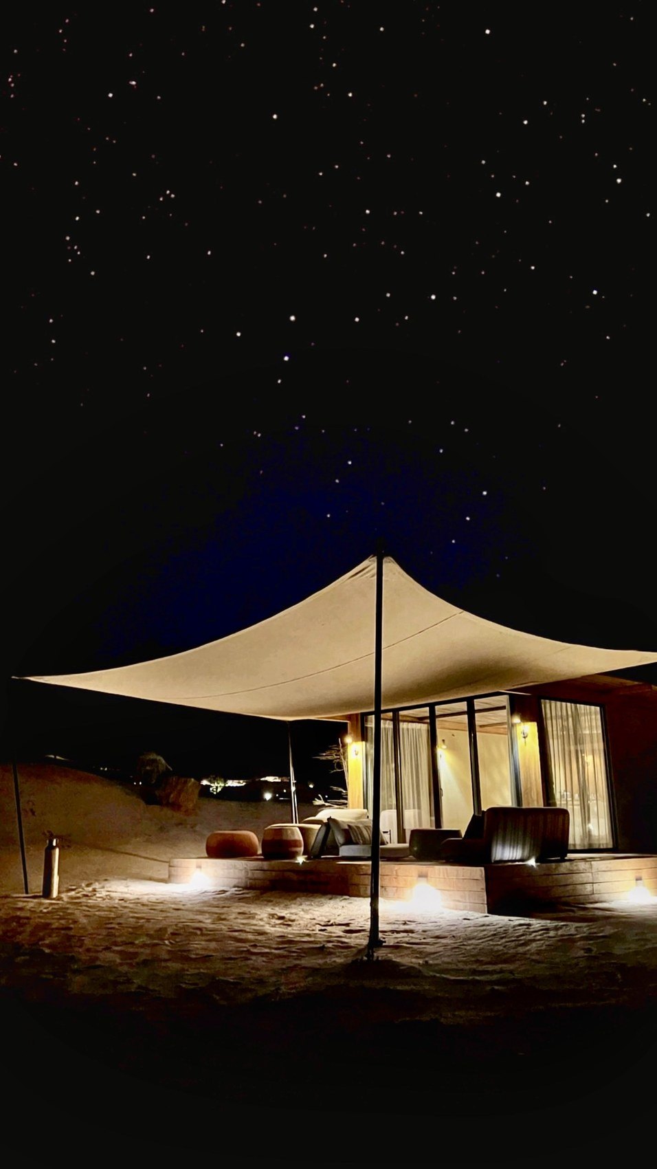 A tented villa at Habitas AlUla lit from within at night under a black sky full of stars