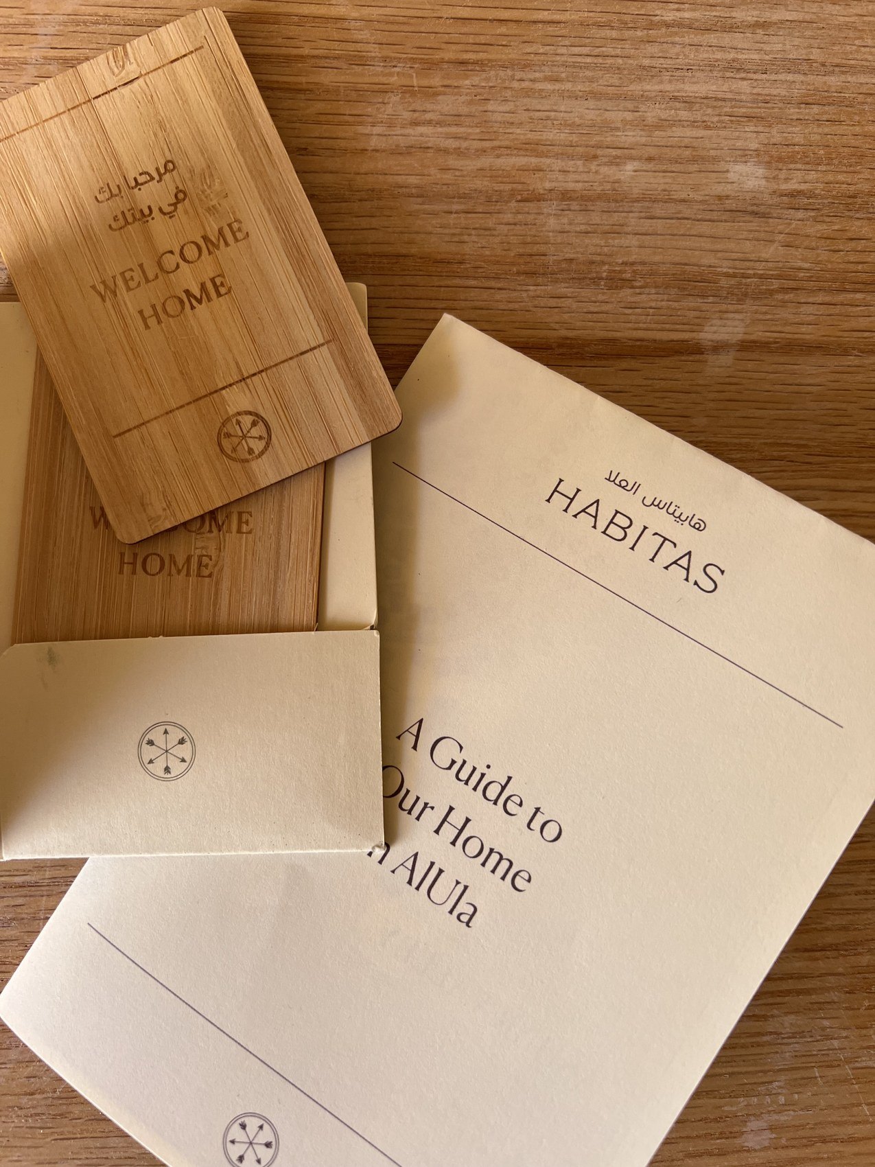 A paper folder printed Habitas and A Guide to Your Home in AlUla beside a wooden Welcome Home key card