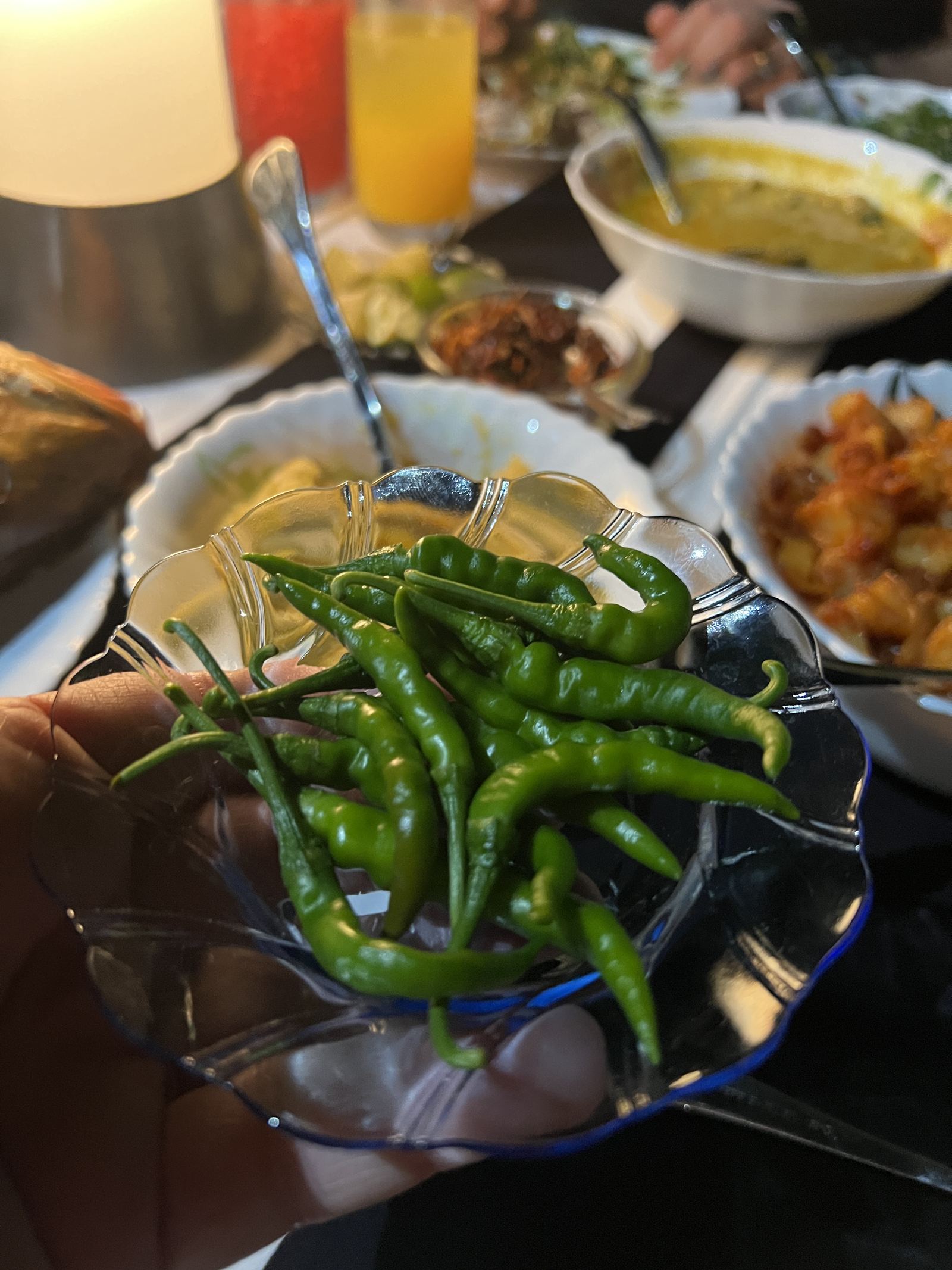A bowl of green chillies held above a spread of Maldivian dishes