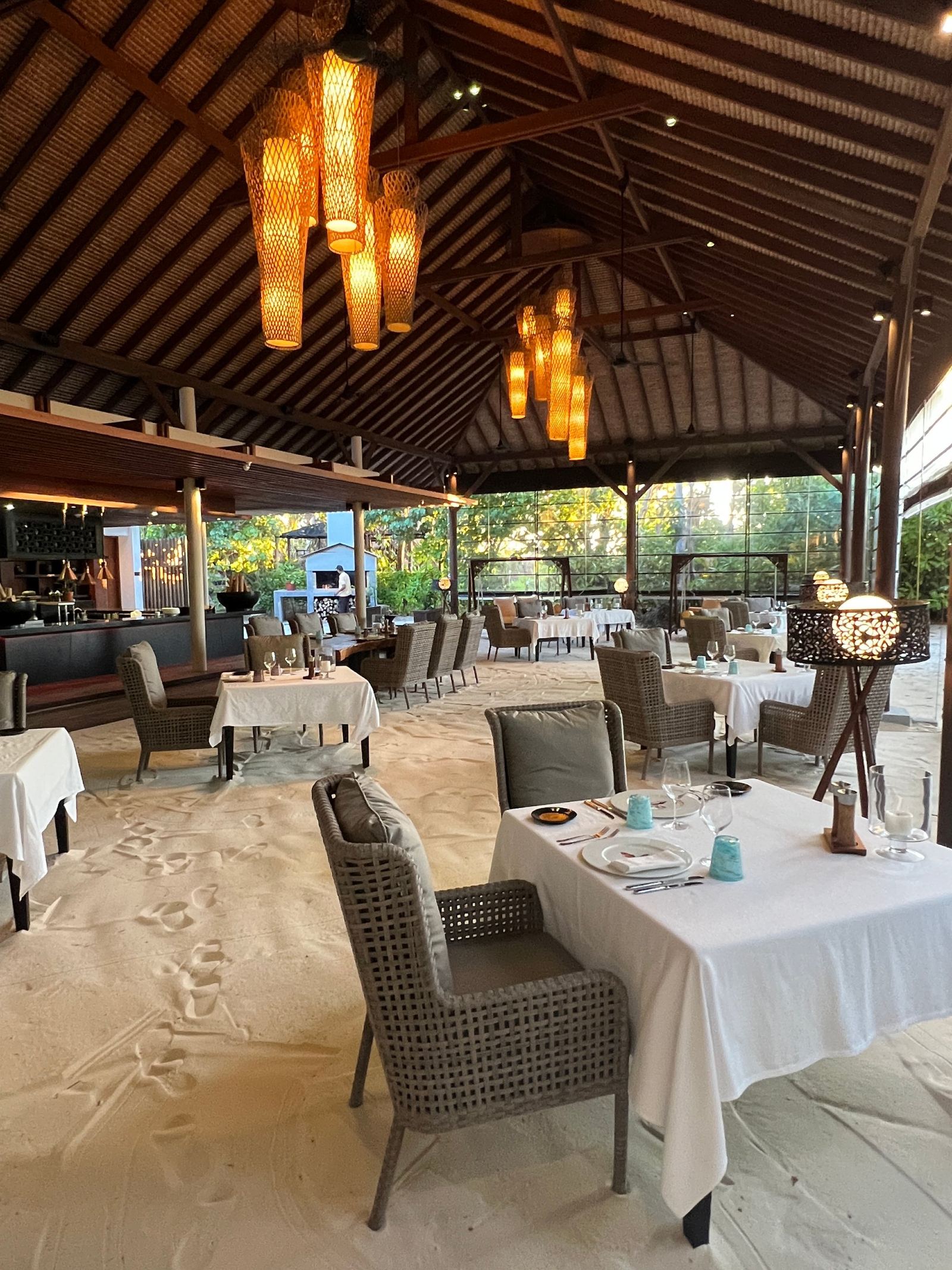 The dining room under its thatched roof, tables laid on a floor of sand