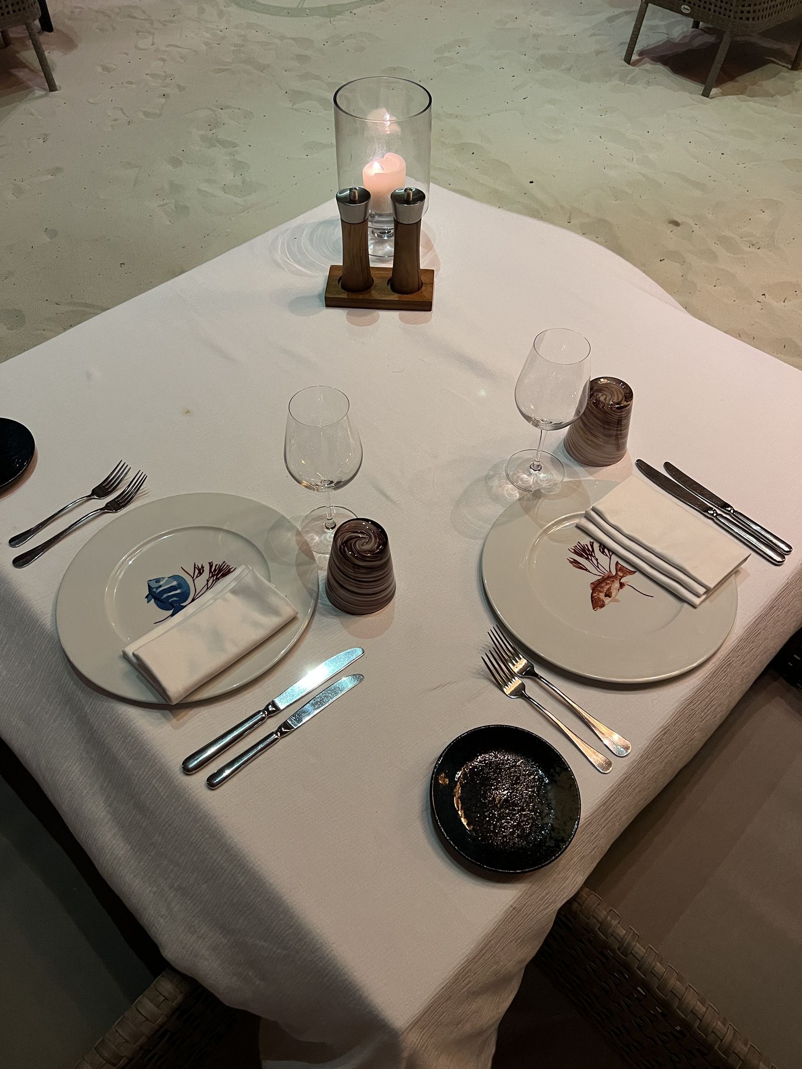 A table laid for dinner on the sand with a candle in a glass