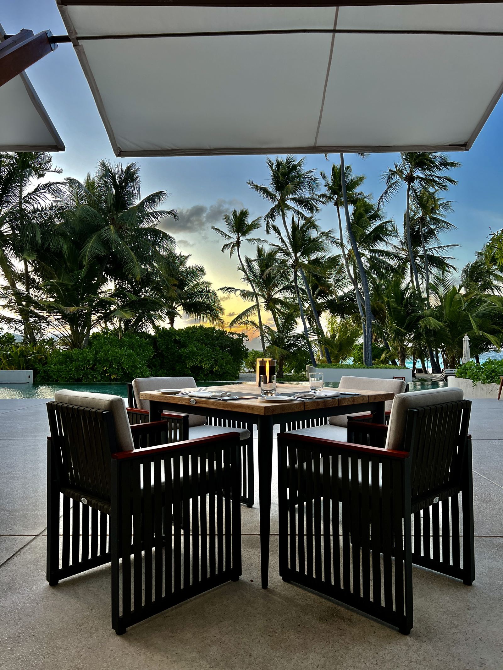 A table laid for dinner under a canopy with the sun going down behind the palms