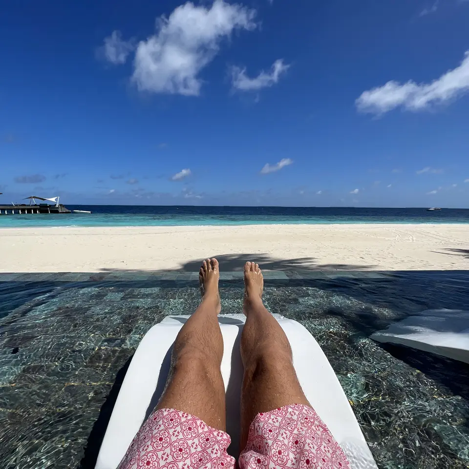 Bare feet on a lounger set in the shallow water at the edge of the pool