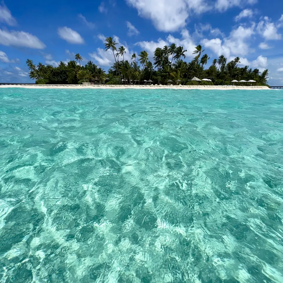 Clear water over sand with the island low on the horizon