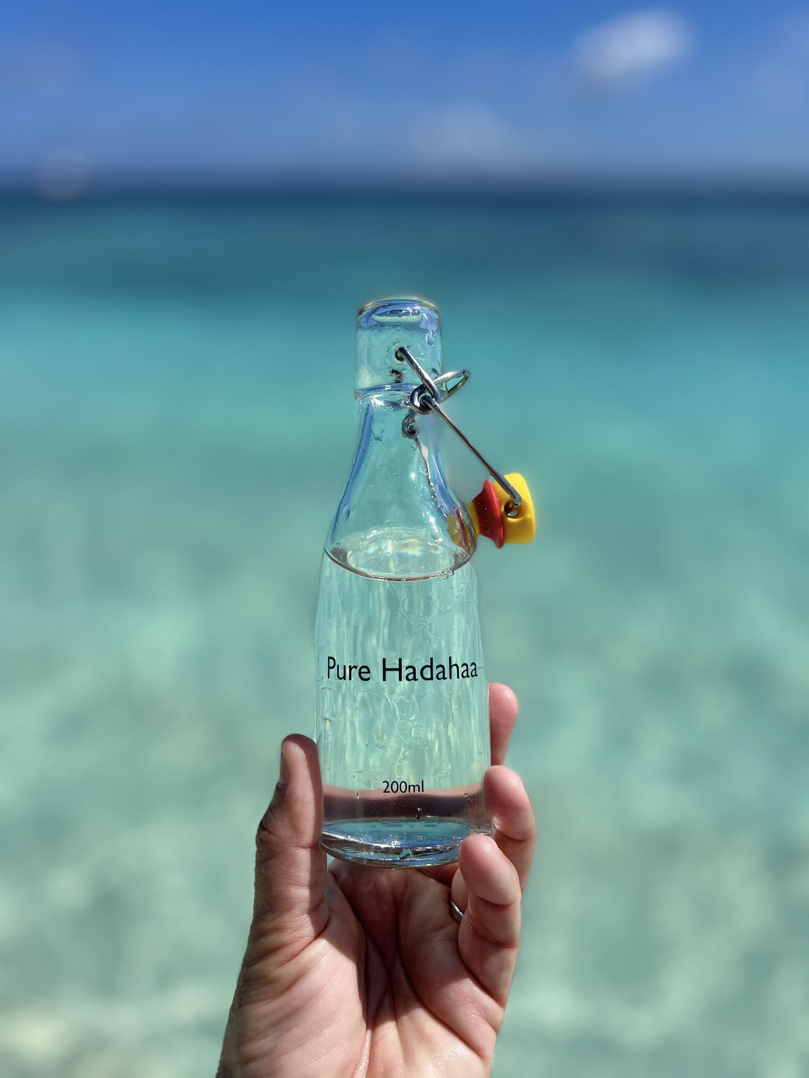 A glass bottle labelled Pure Hadahaa held up against the lagoon
