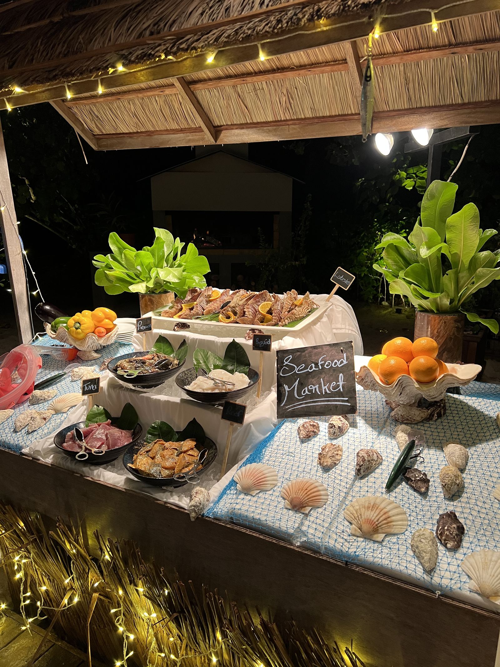 A seafood market display laid out under a thatched roof at night